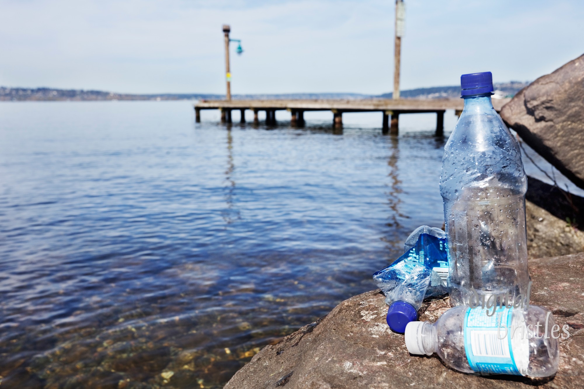 Disposable plastic water bottles sitting on a rock by a clean lake