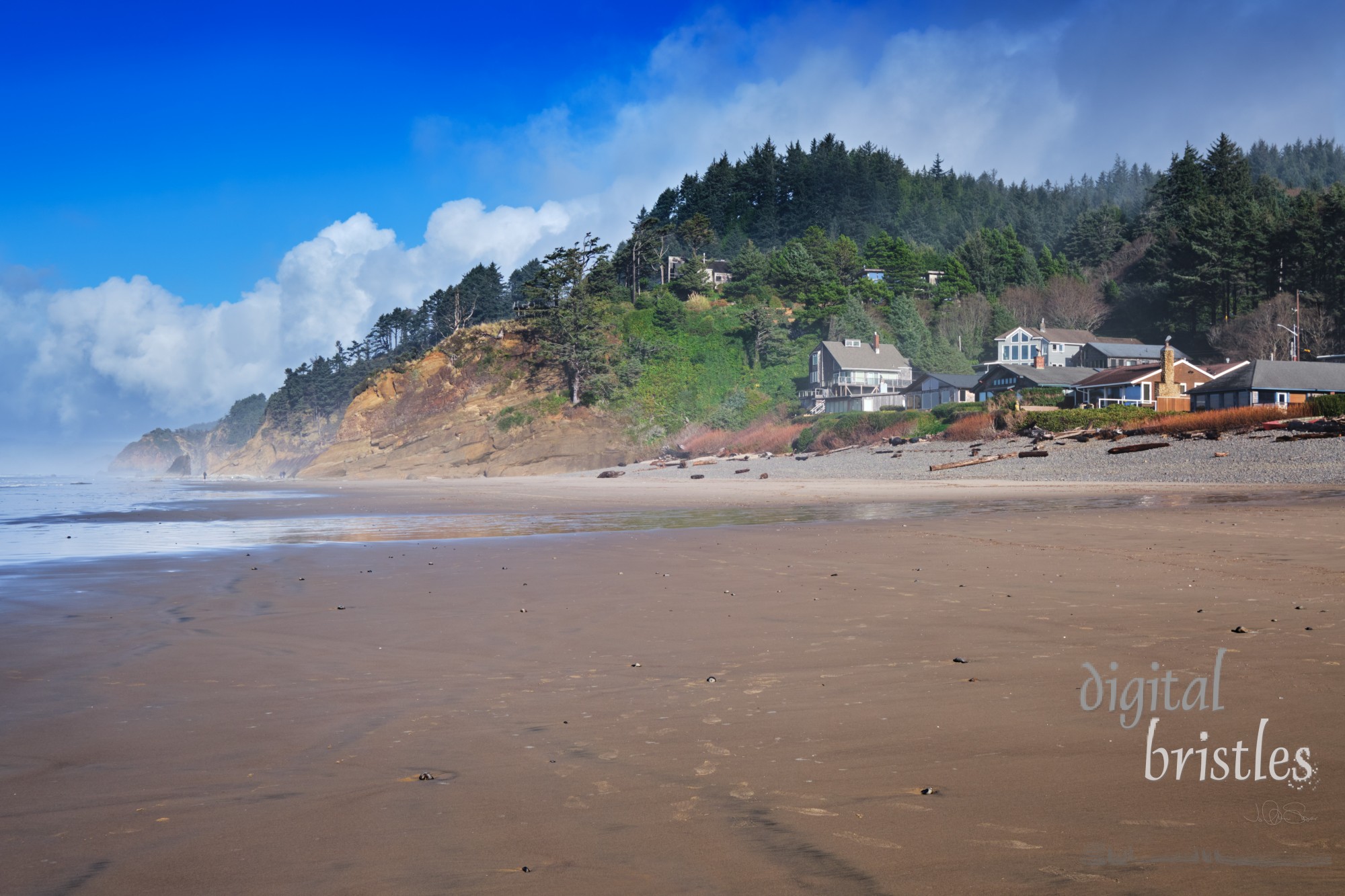 Wild and rocky Oregon coast with beach houses perched on the rocks and above the wide sandy beach. Arch Cape, Oregon, looking north to Hug Point and Cannon Beach