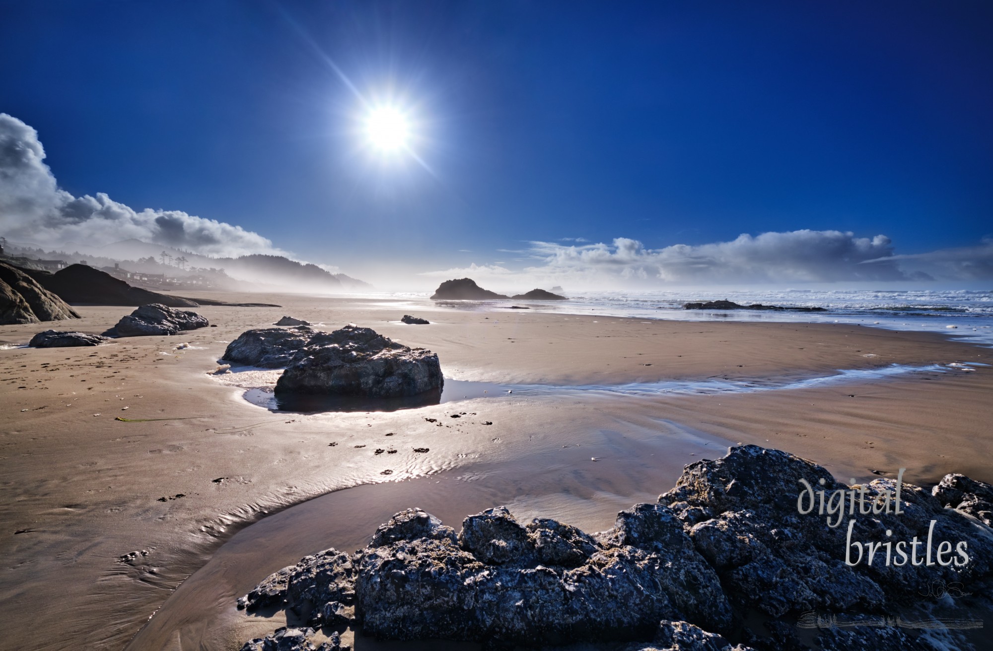 Bright sun shines through mist at low tide in Arch Cape, Oregon, on a pretty Winter afternoon