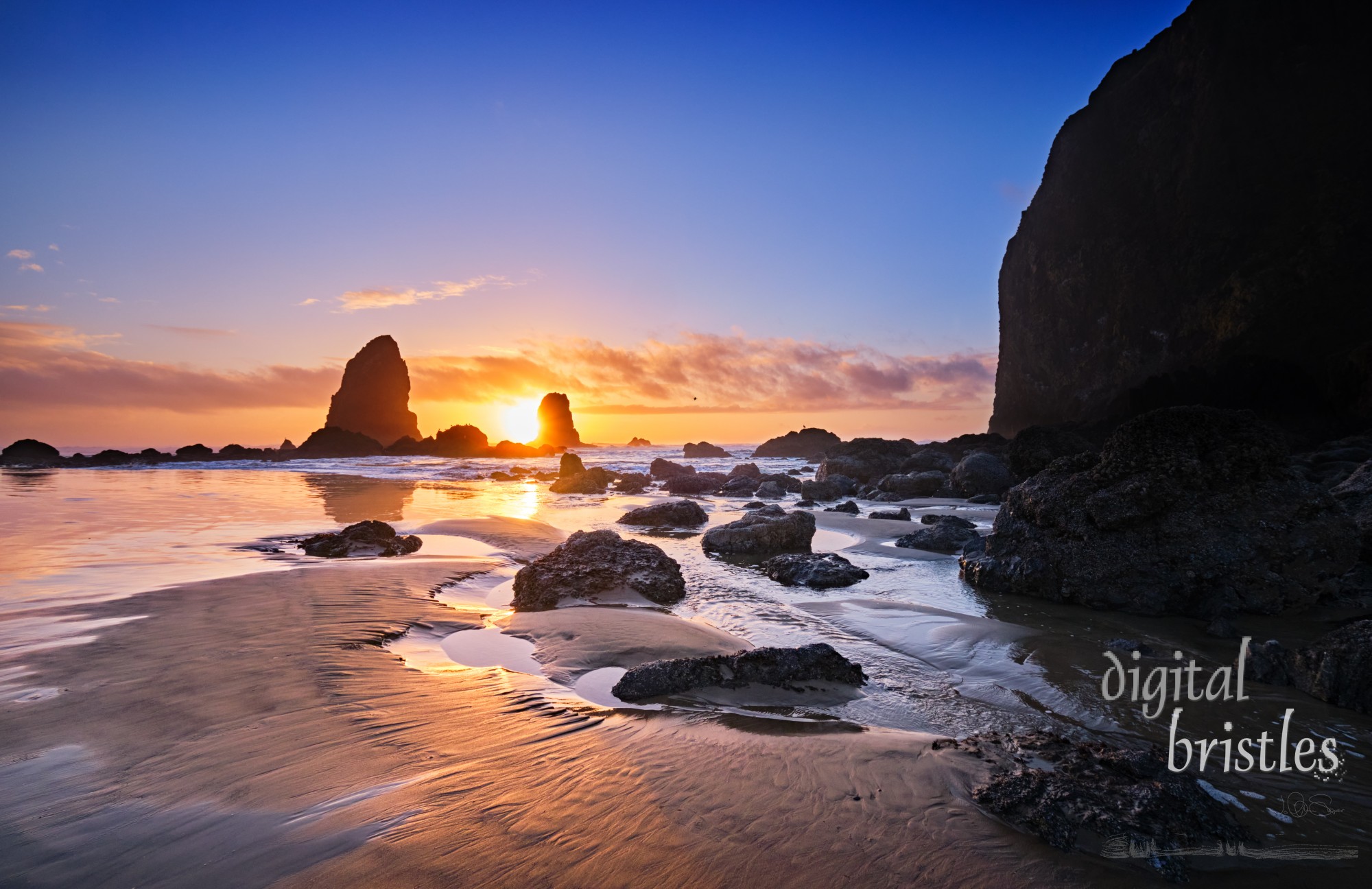 Wintry sun sets behind the Needles at Haystack Rock, Cannon Beach, Oregon, at low tide