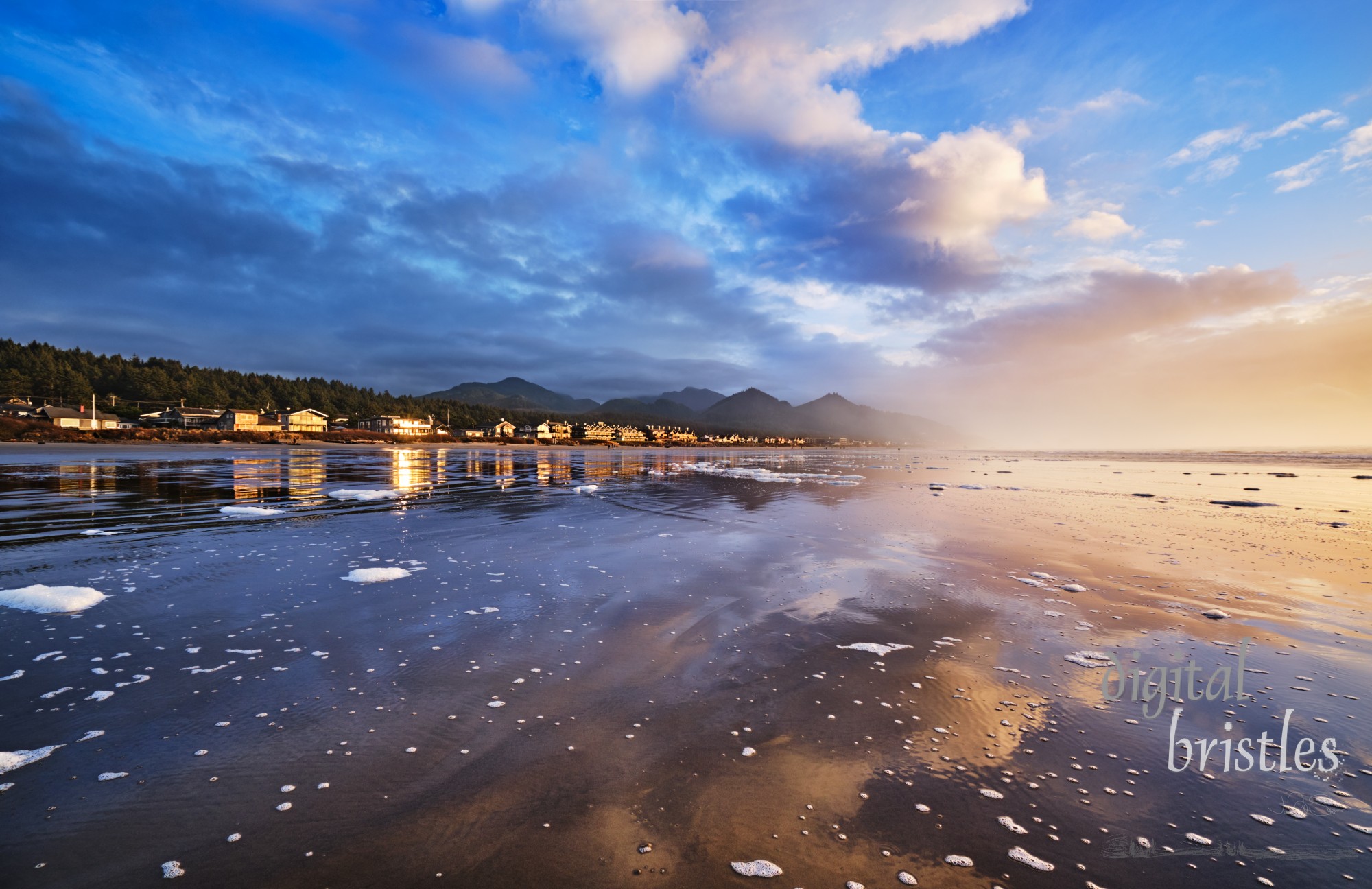 Winter sunset at low tide at Cannon Beach, Oregon. Looking south to Arch Cape in the mist over a beach strewn with sea foam 