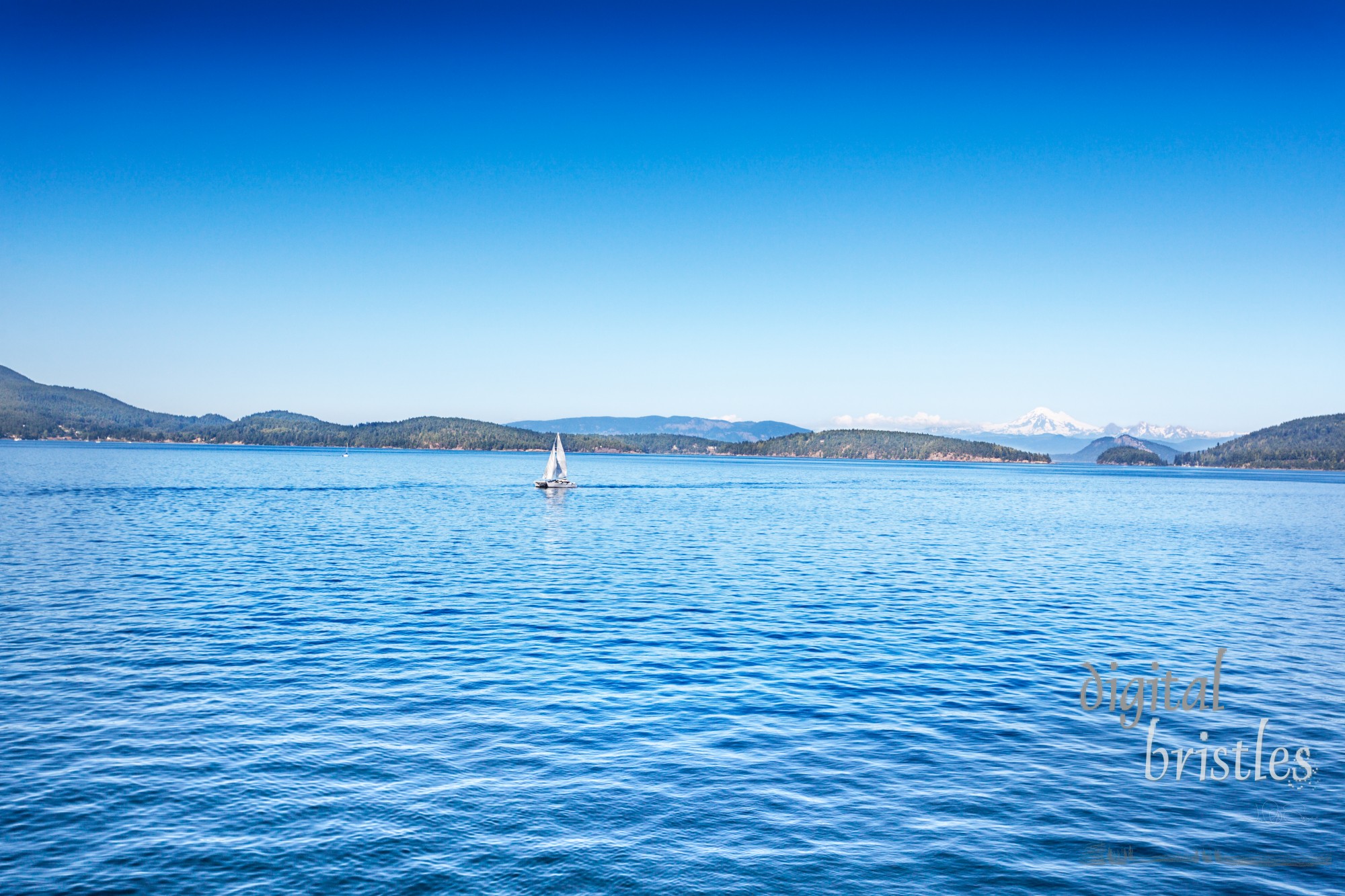 Sailboat heads throgh the San Juan Islands with Mount Baker and the cascades visible on the mainland