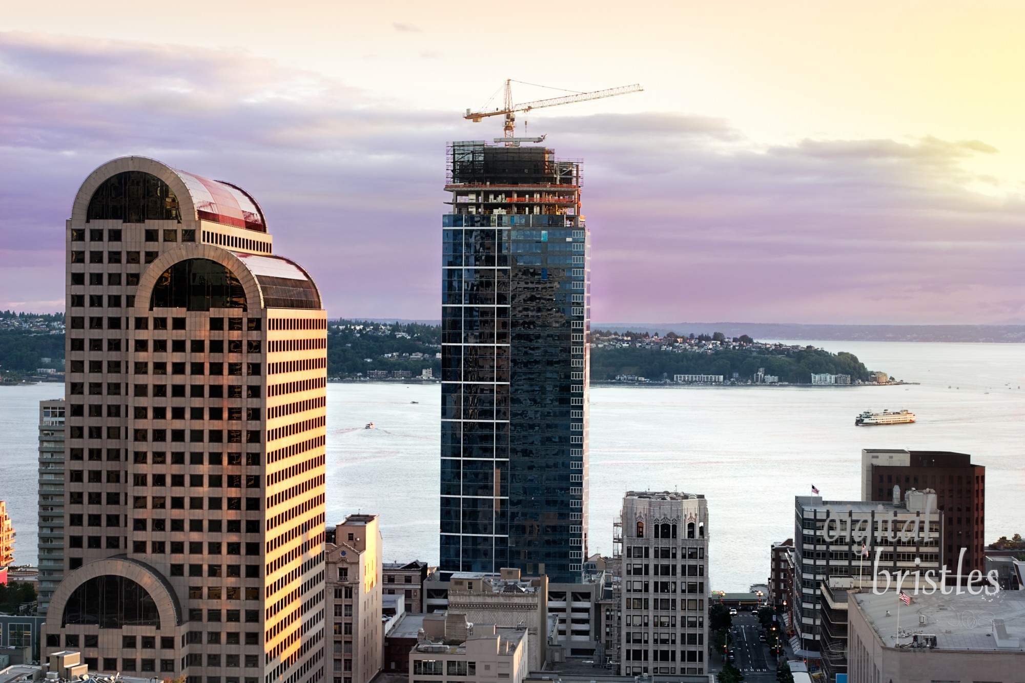 Sun goes down over Elliott Bay and Seattle's cranes and construction, boats and ferries still criss crossing Puget Sound