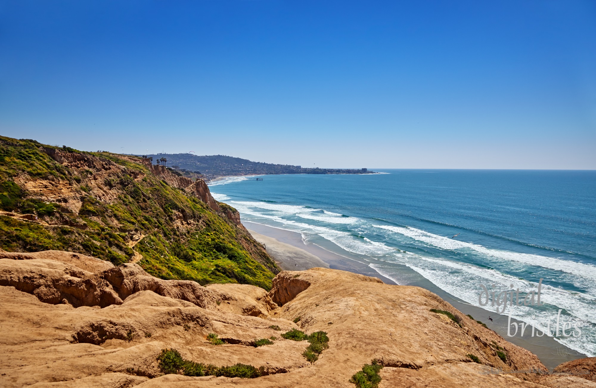 Steep, eroded cliffs with a zigzag path to Black's Beach, California. Scripps Pier and La Jolla Cove in the distance