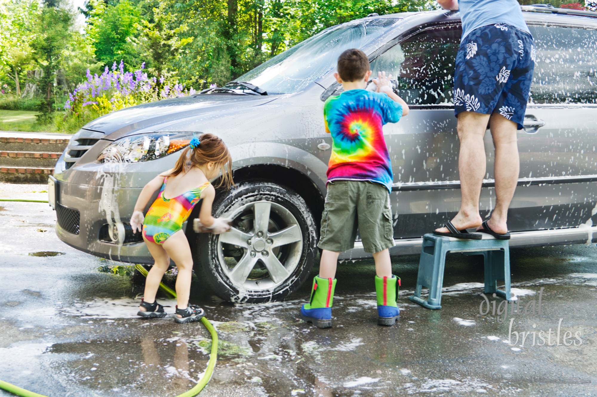 Brother & sister help Dad with washing a car in the driveway