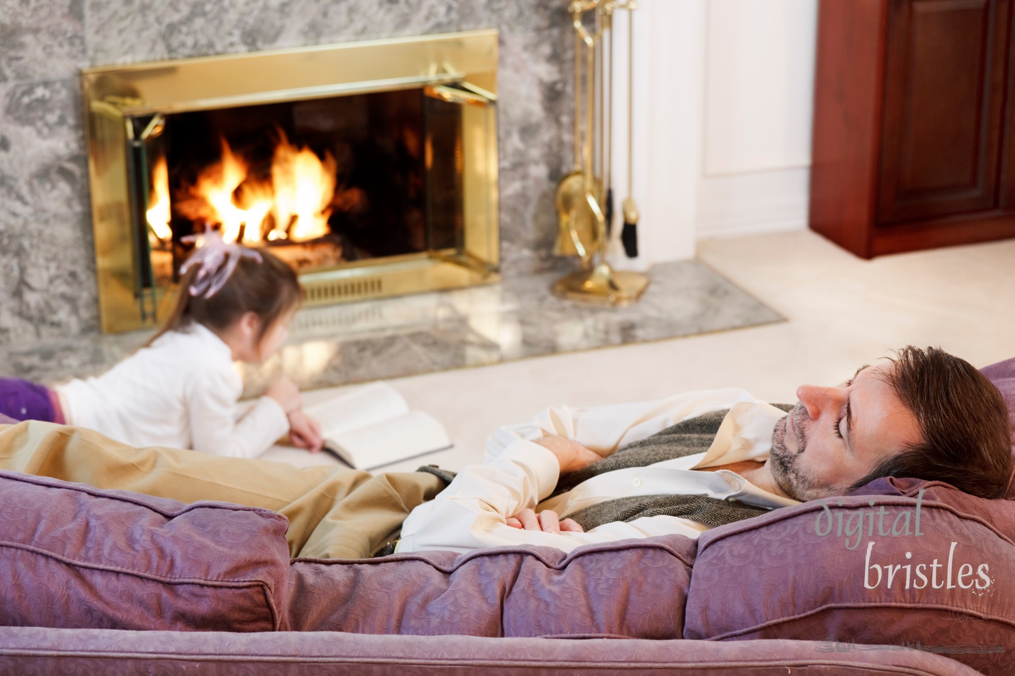 Little girl reads by the fire while Dad naps