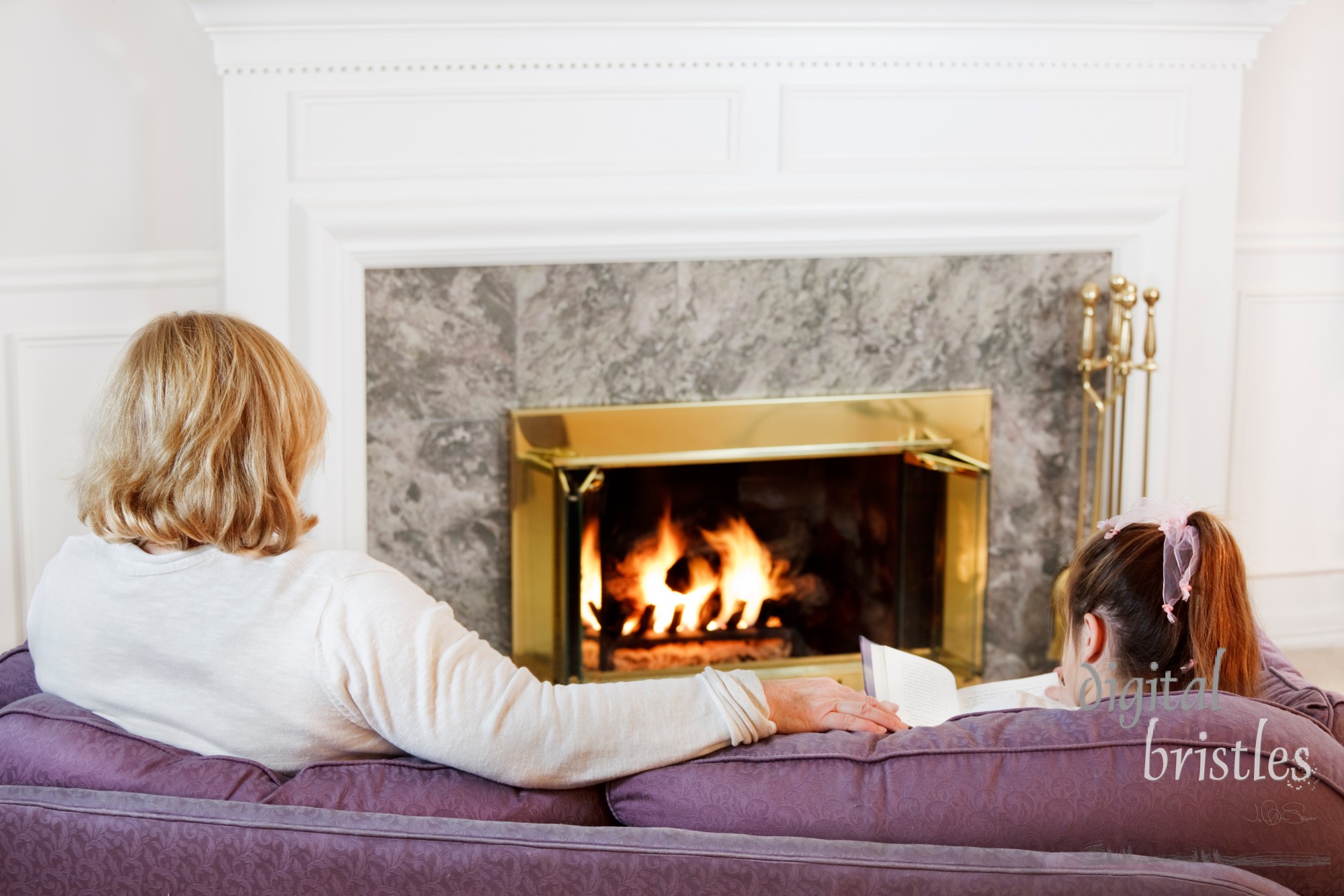 Mother and daughter sit on the sofa  to read by the fire