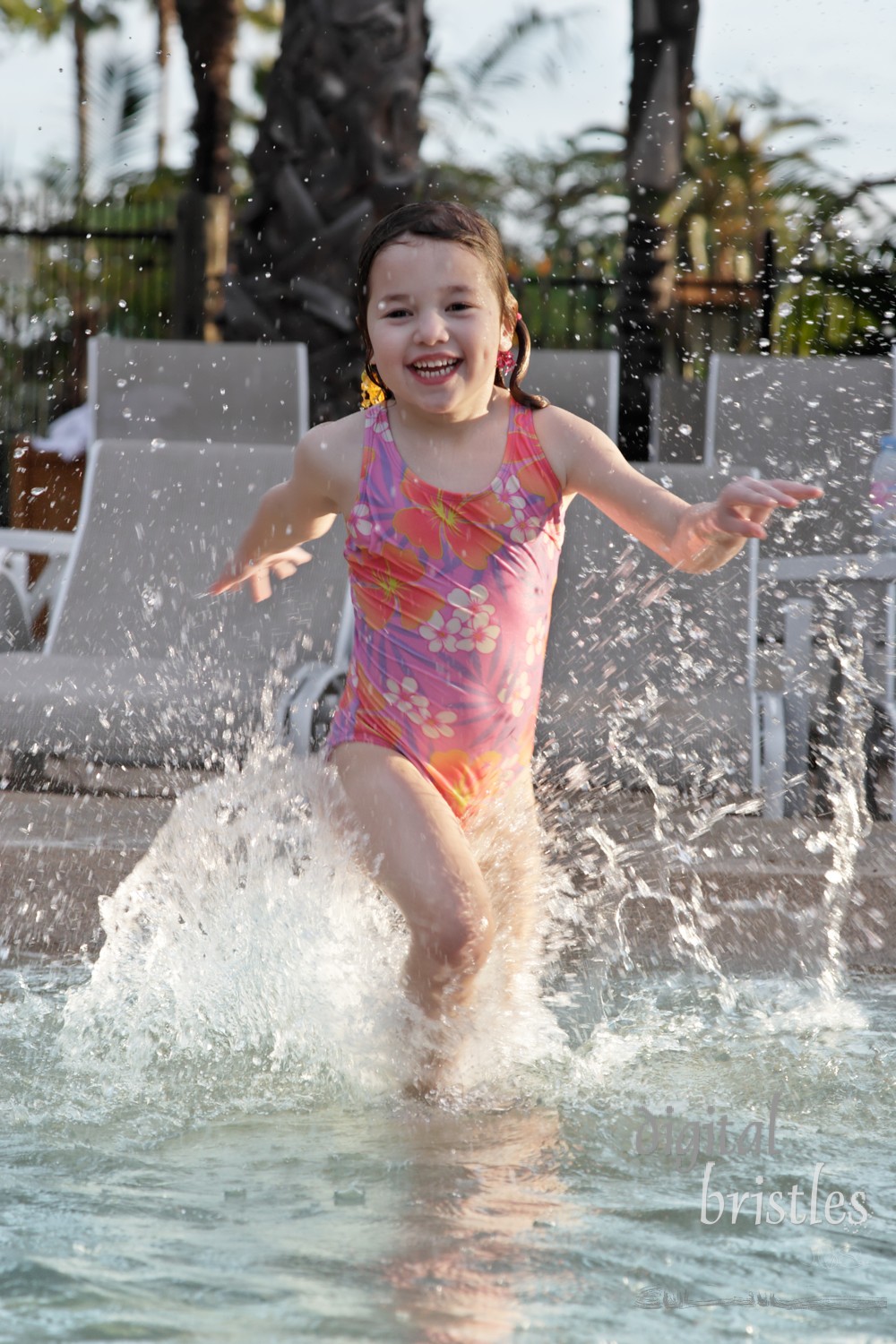 Young girl splashes excitedly into the pool