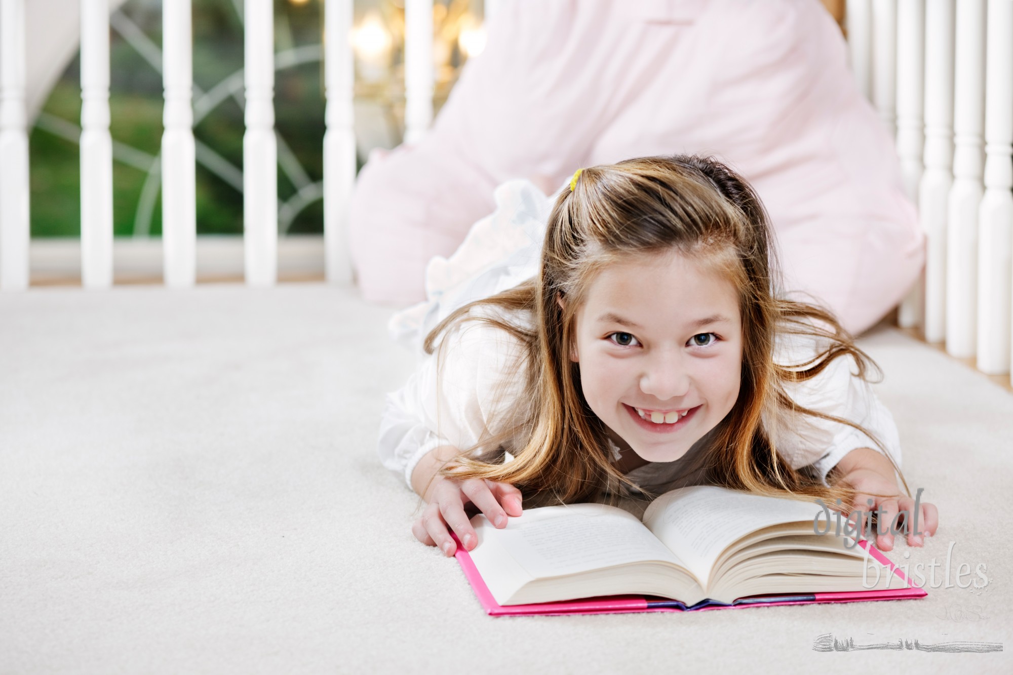 Young girl lying on the floor looks up from her reading and smiles