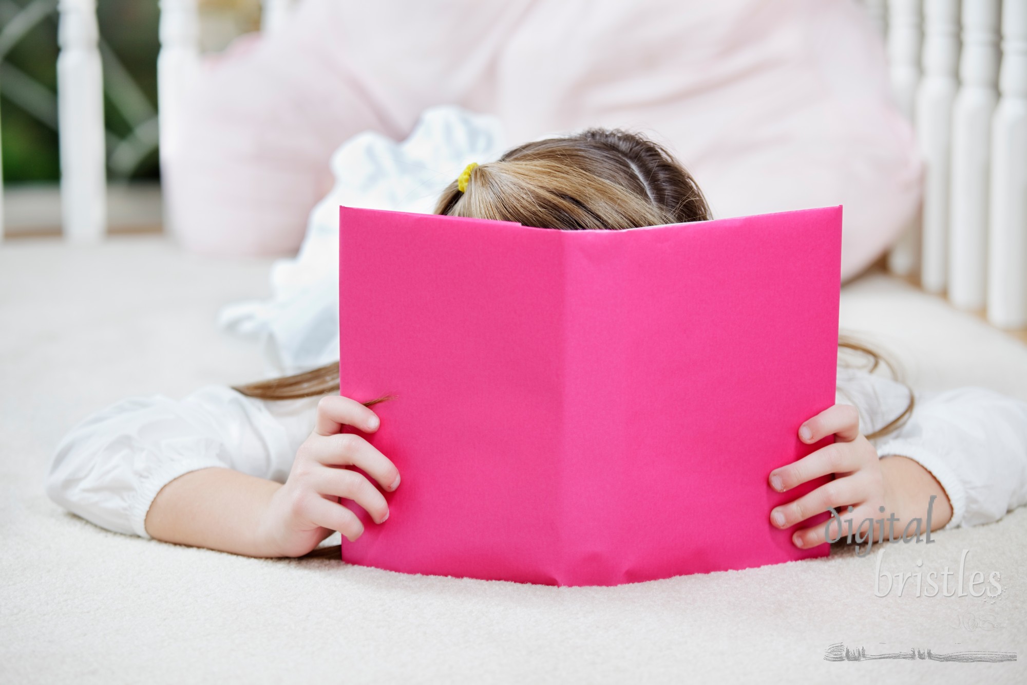 Young girl lying on the floor reading, hiding behind her book