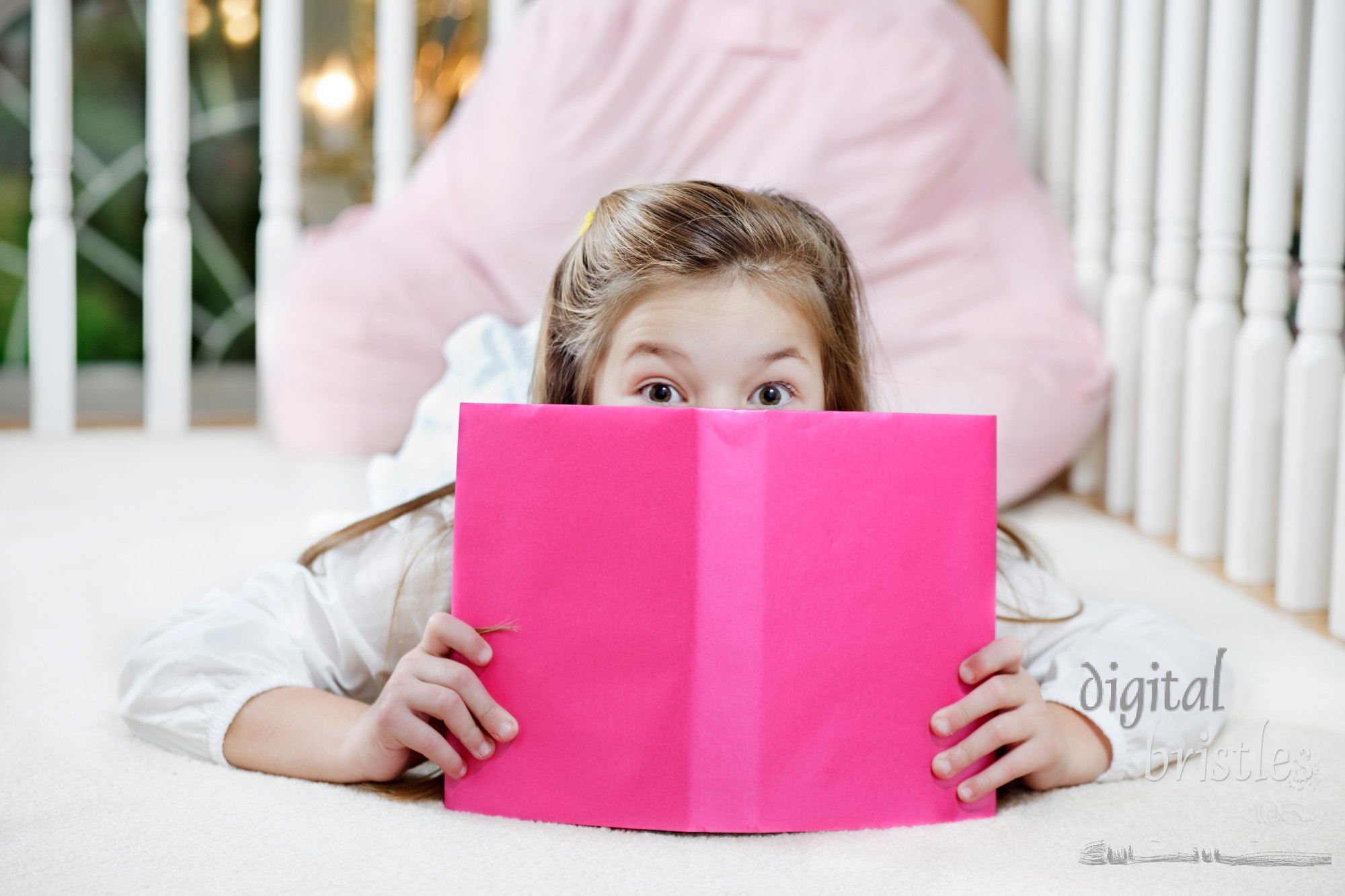 Young girl lying on the floor reading, peeking over her book