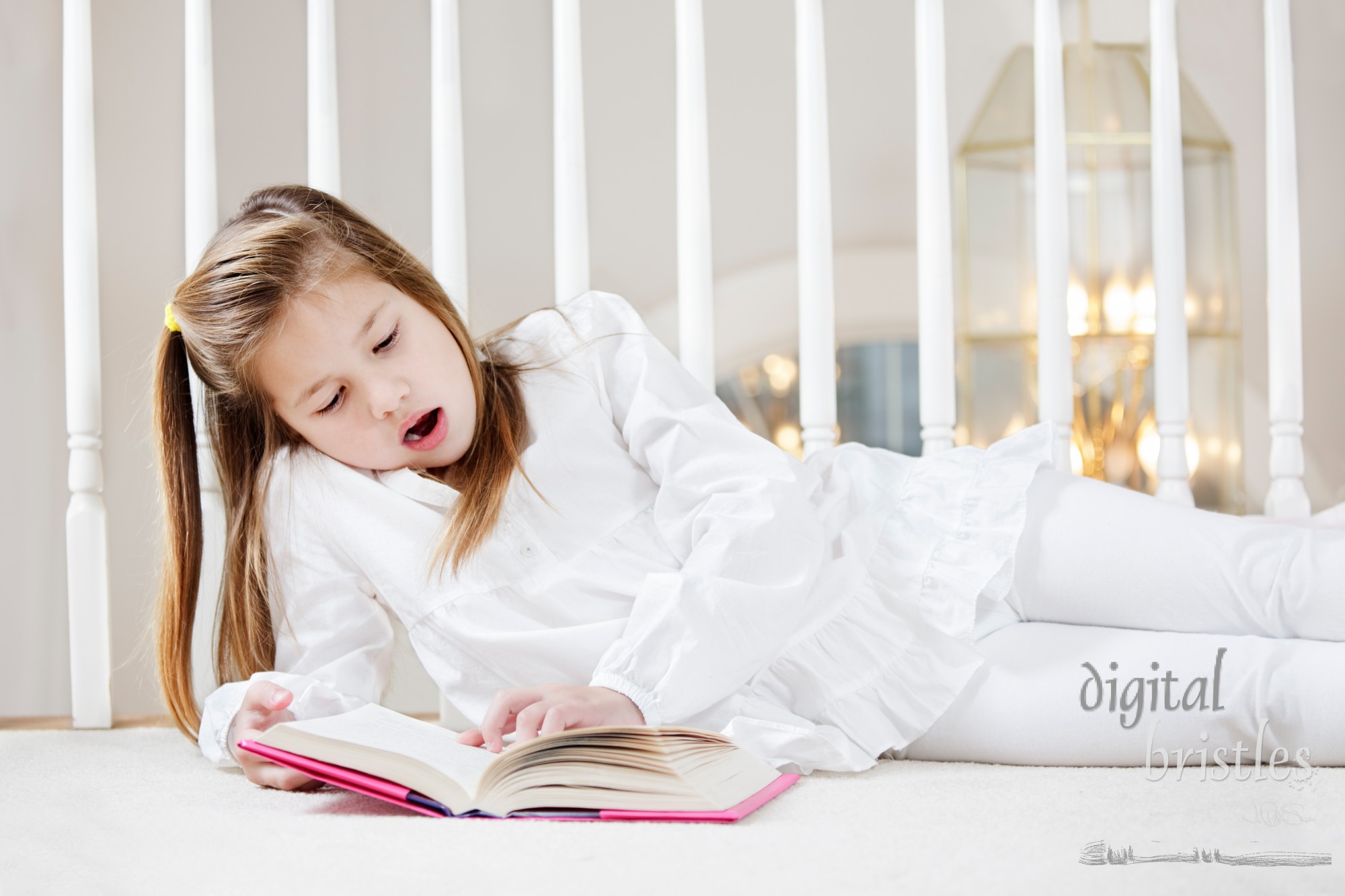 Young girl starts to yawn as she's lying on the floor reading