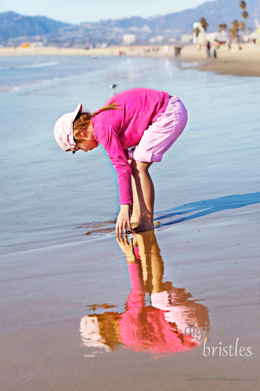 Young girl and her reflection playing on the beach near the water