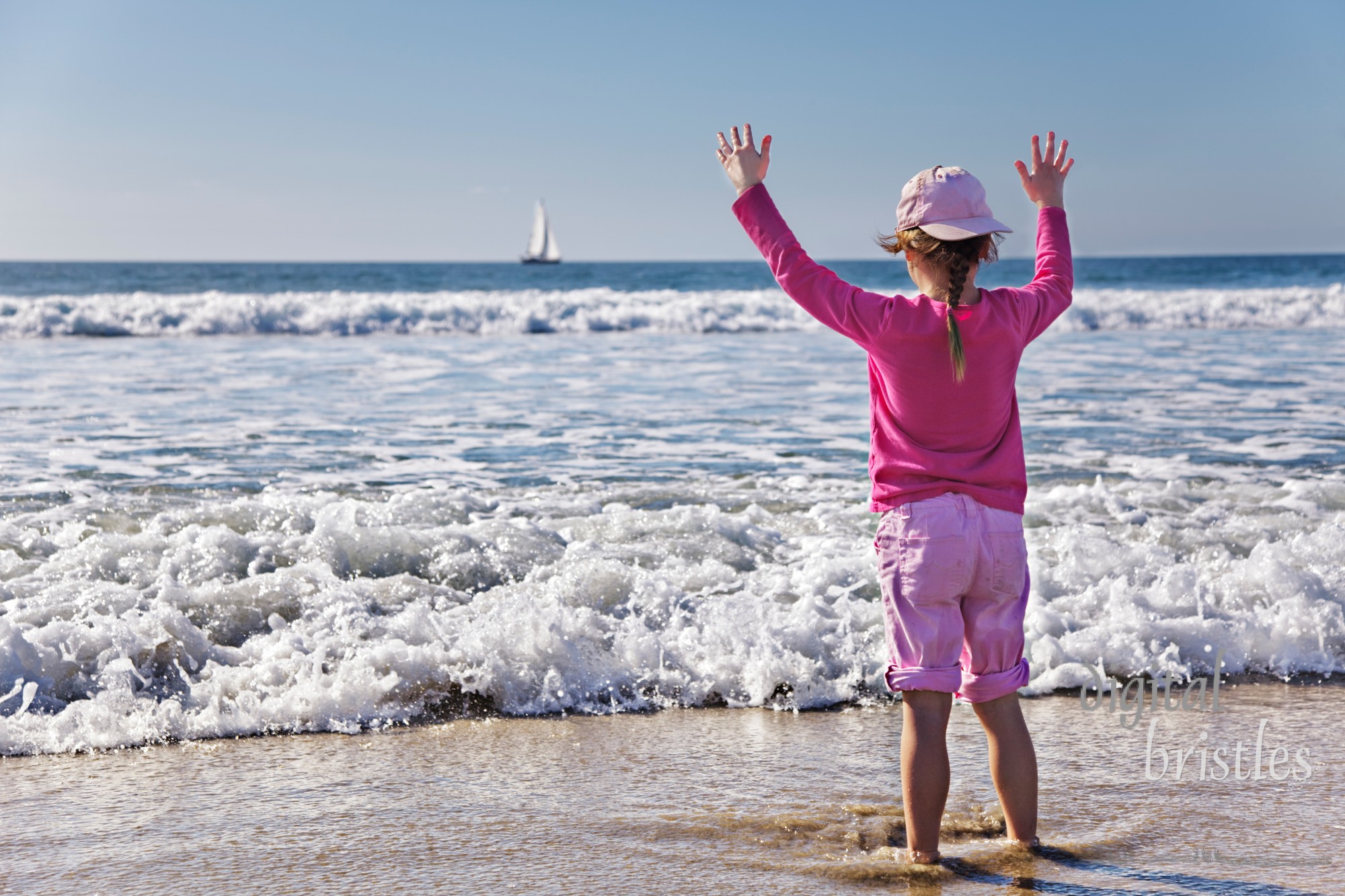 Young girl holds up hands as wave approaches her