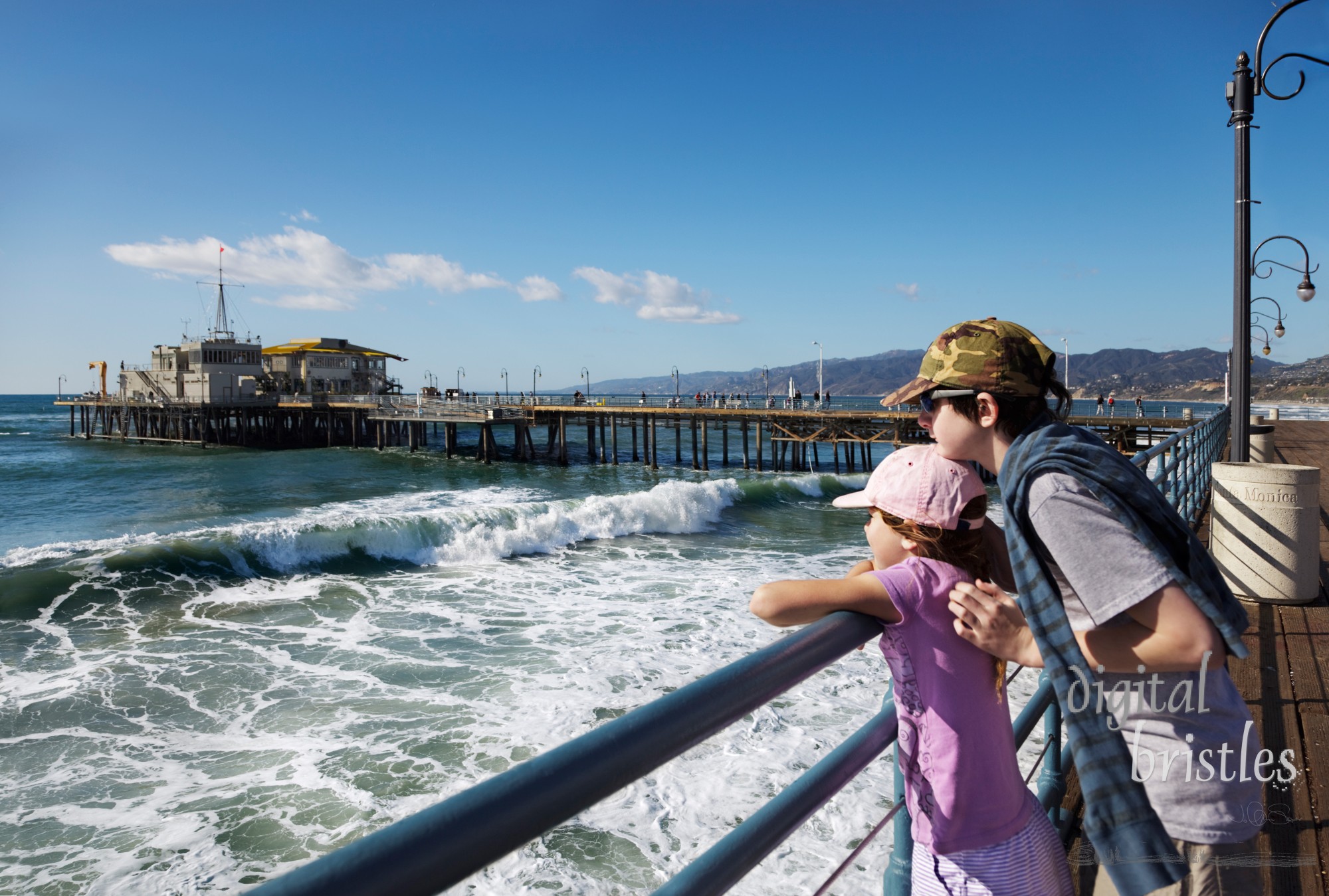 Brother holds his sister as they watch the waves from the end of the pier