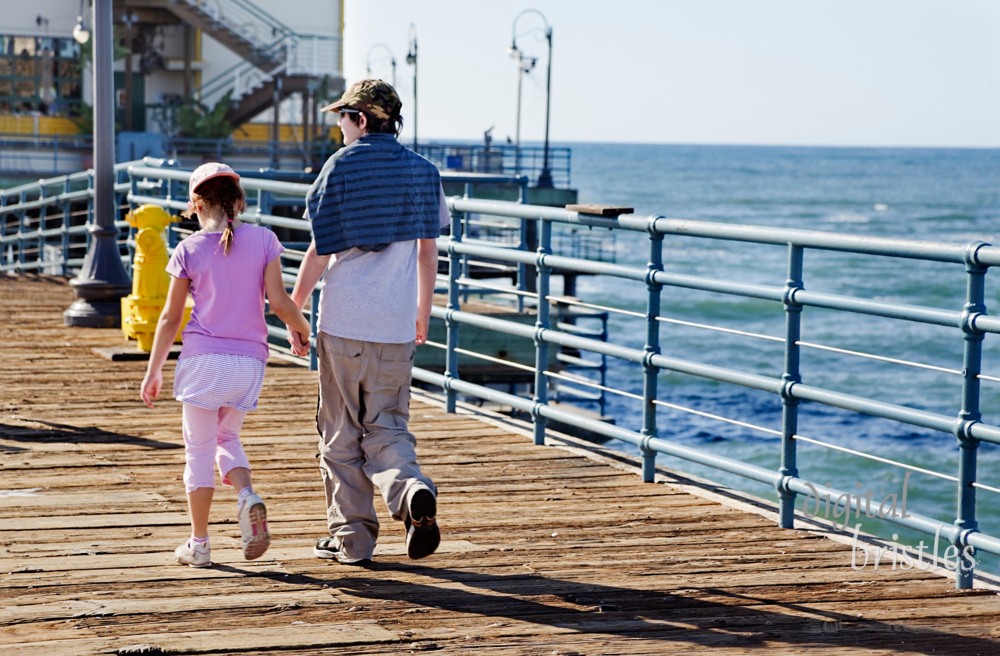 Brother & sister hold hands as they walk along the pier