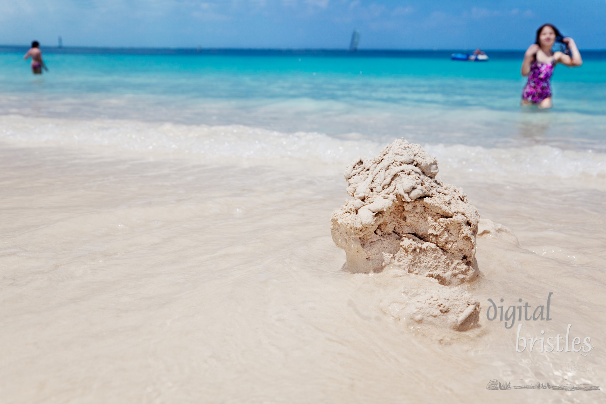 Young girl walks back to inspect her sandcastle being washed away by the gentle waves of Grace Bay, Turks & Caicos