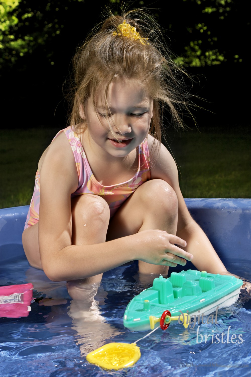 Young girl smiles as sheplays with toys in a paddling pool