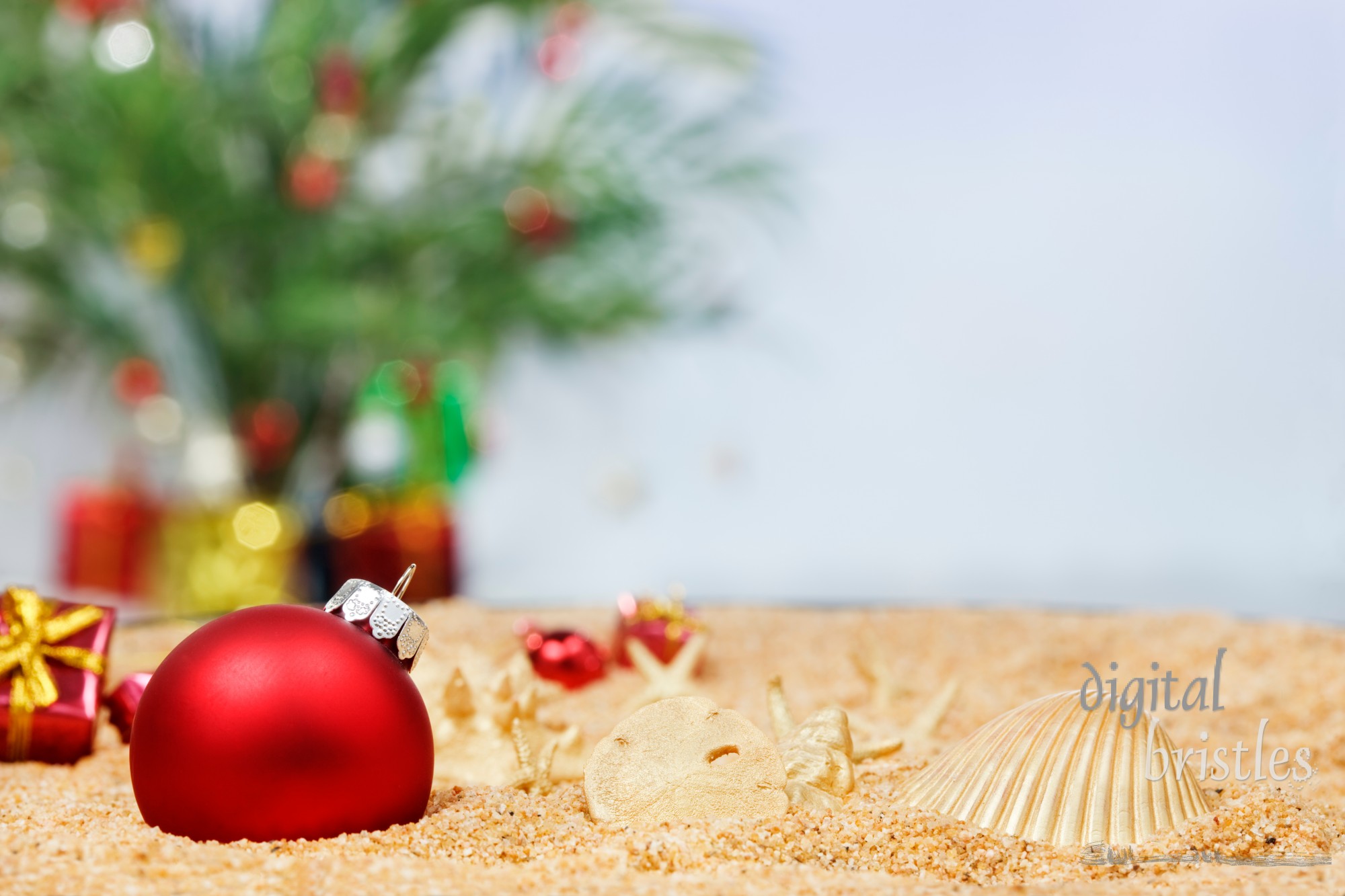 Christmas ornaments in the sand with a palm decorated for the season in the background