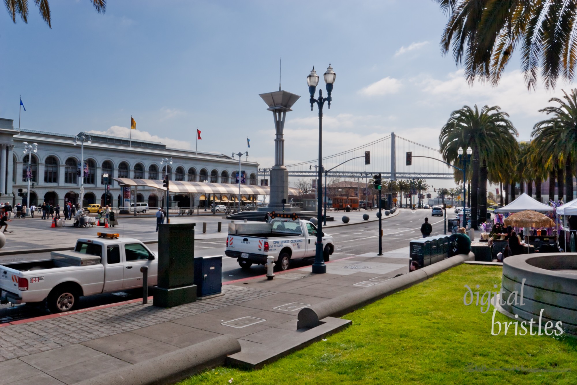 The Embarcadero with Ferry Building across the street and San Francisco-Oakland Bay Bridge in the distance.  On a Winter morning, tourists and business mix on this busy street on the waterfront. Taken from Justin Herman Plaza.