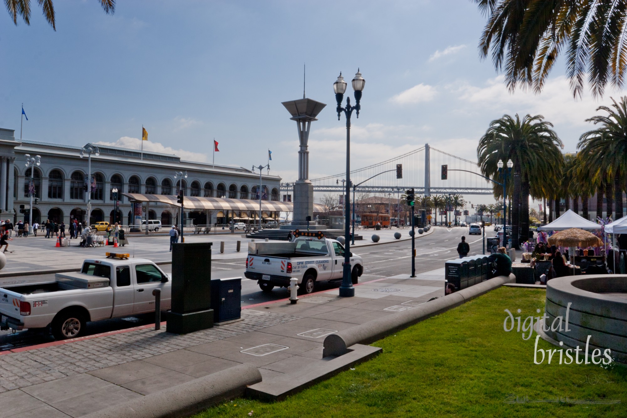 The Embarcadero with Ferry Building across the street and San Francisco-Oakland Bay Bridge in the distance.  On a Winter morning, tourists and business mix on this busy street on the waterfront. Taken from Justin Herman Plaza.