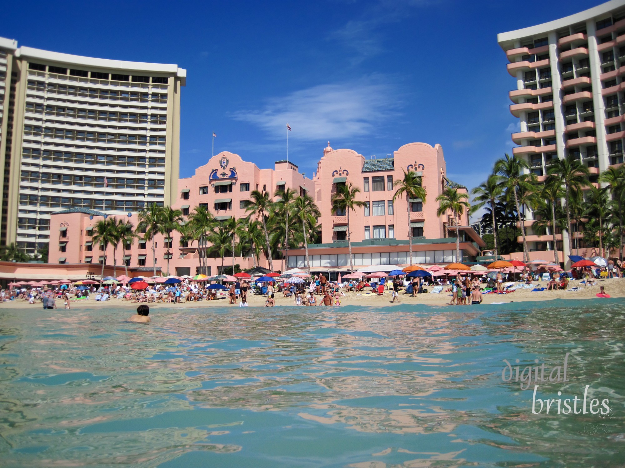 Tourists enjoying the sun on Waikiki Beach outside the Royal Hawaiian Hotel, Honolulu, Hawaii. The distinctive coral pink hotel was built in 1927 and rennovated in 2009. The modern Royal Beach Tower - pink balconies on the hotel's left - is part of the hotel, added in 1969.