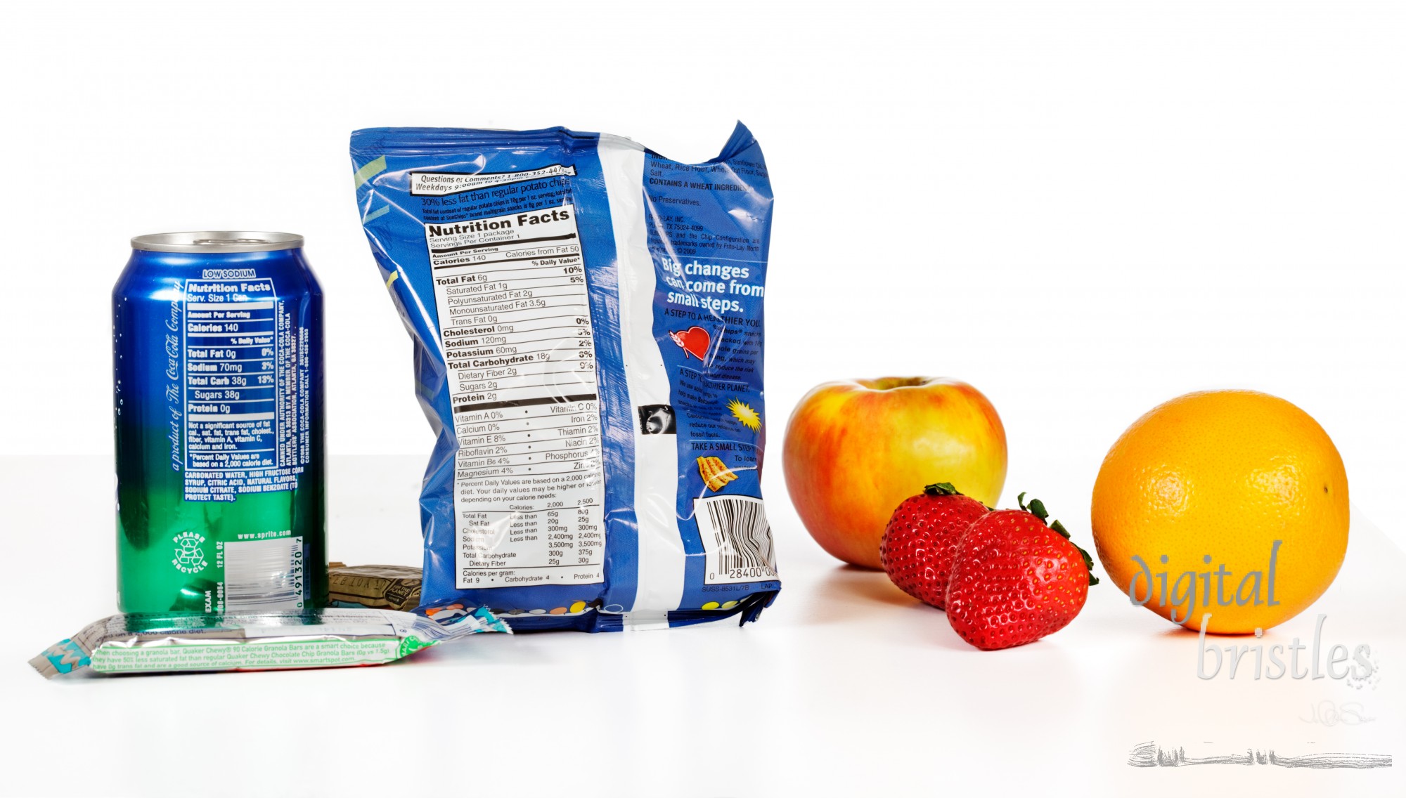 Healthy versus unhealthy food choices for snacks. Nutrition labels for a can of Sprite, bag of Sun Chips and a granola bar and Cliff bar on the table. Fresh fruit - apple, strawberries or an orange - as an alternative choice.