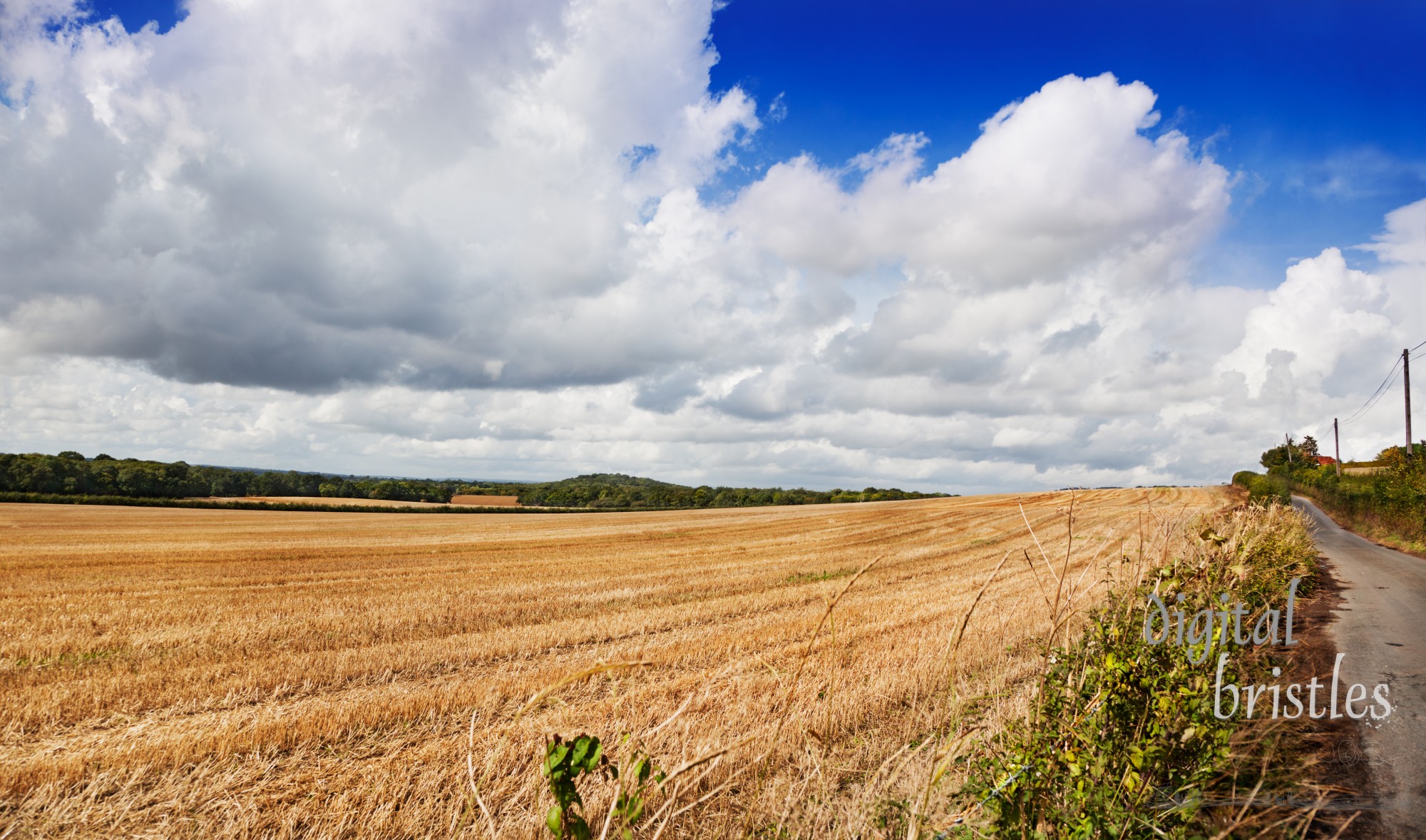 Deserted country road runs beside a newly cut field on a a sunny late summer afternoon, Hollingbourne, Kent, UK