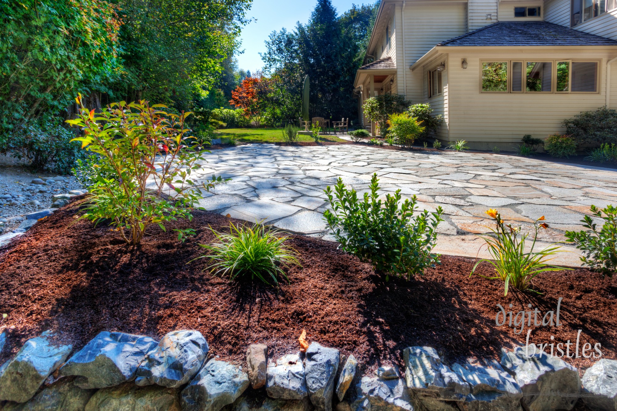 Completed stone patio and a new flower bed at one side of a sunny back garden