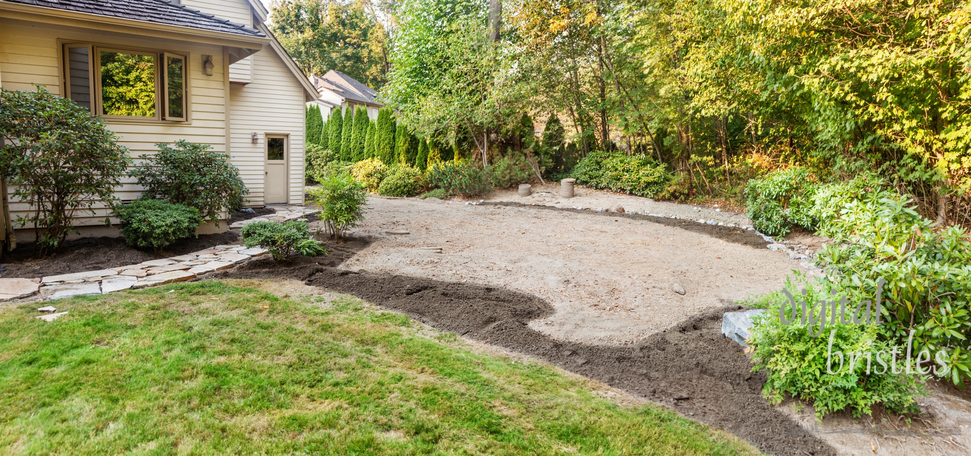 Patio area marked out with topsoil placed on flower bed areas and stone retaining wall built around the far edge