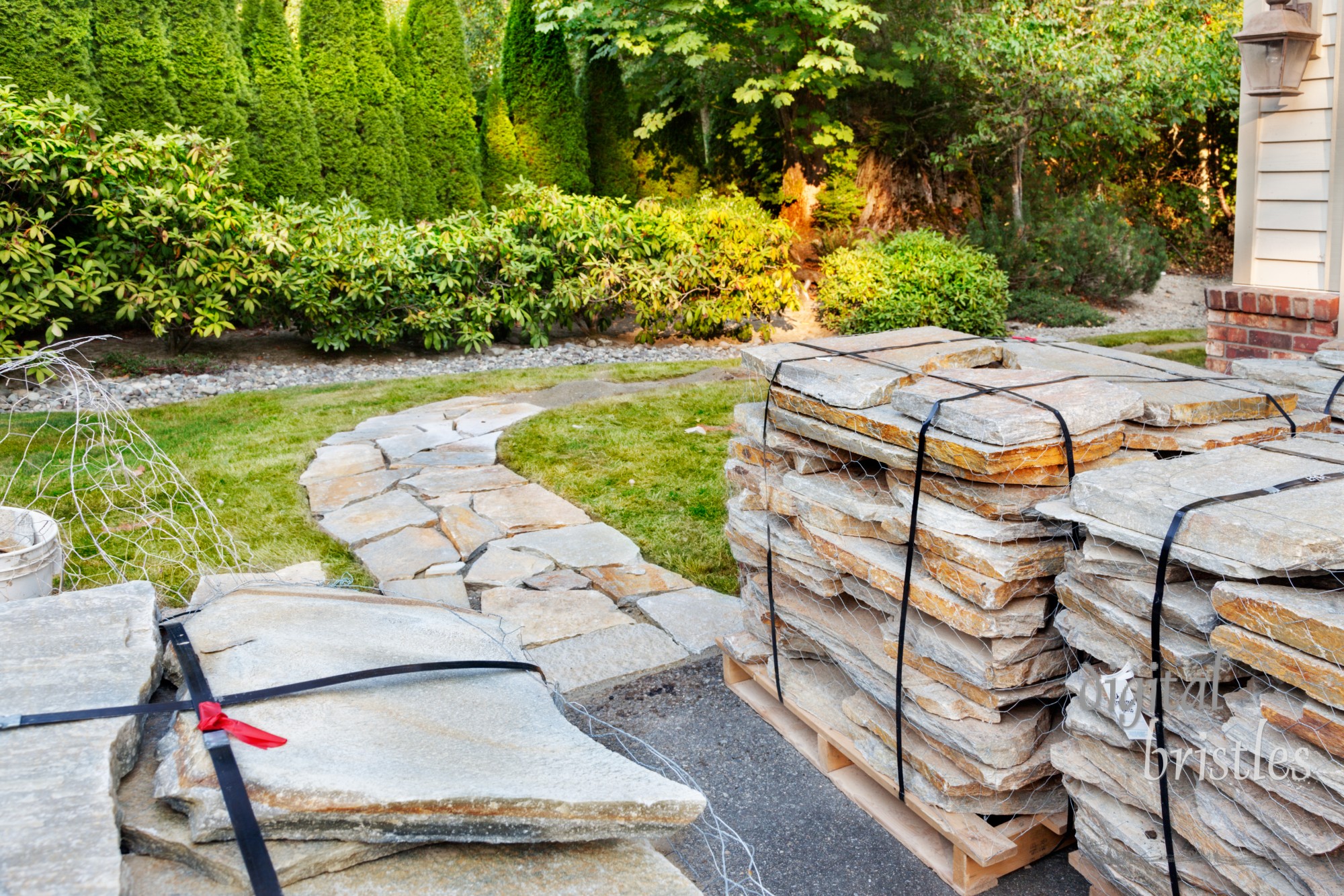 Pallets of stone, secured with wire and straps, sit by the beginnings of a garden path