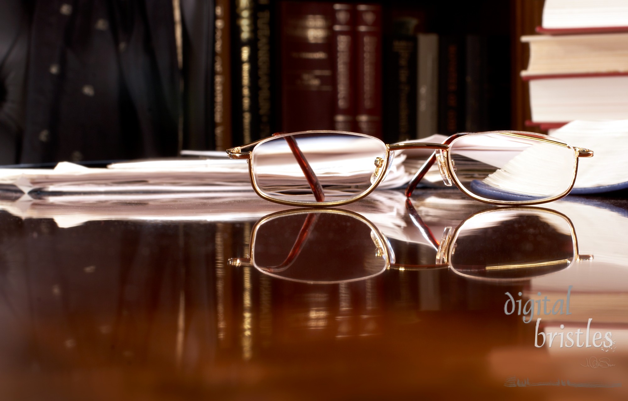 Reading glasses on desk piled with work. Focus is on glasses