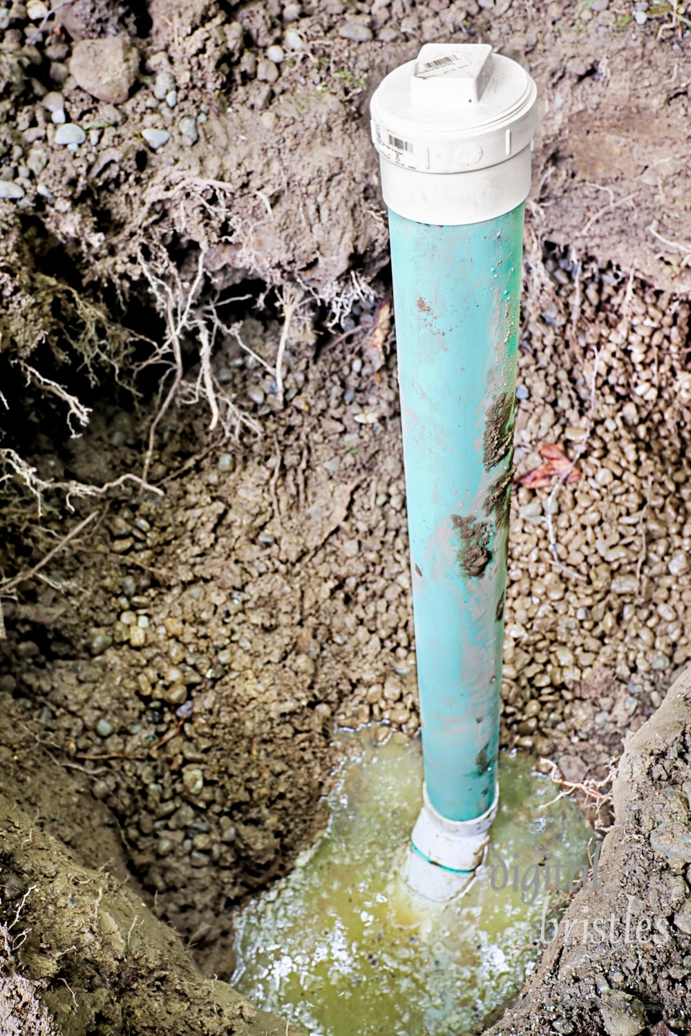 Groundwater in hole being dug for yard drainage. Focus on top of pipe & cap