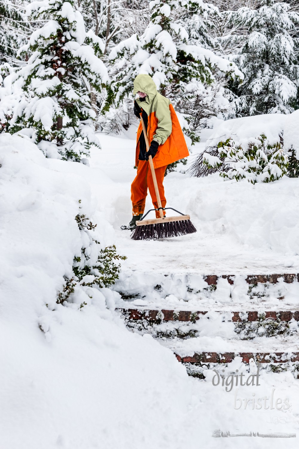 Boy uses a push broom to sweep snow off a front path and steps of his house