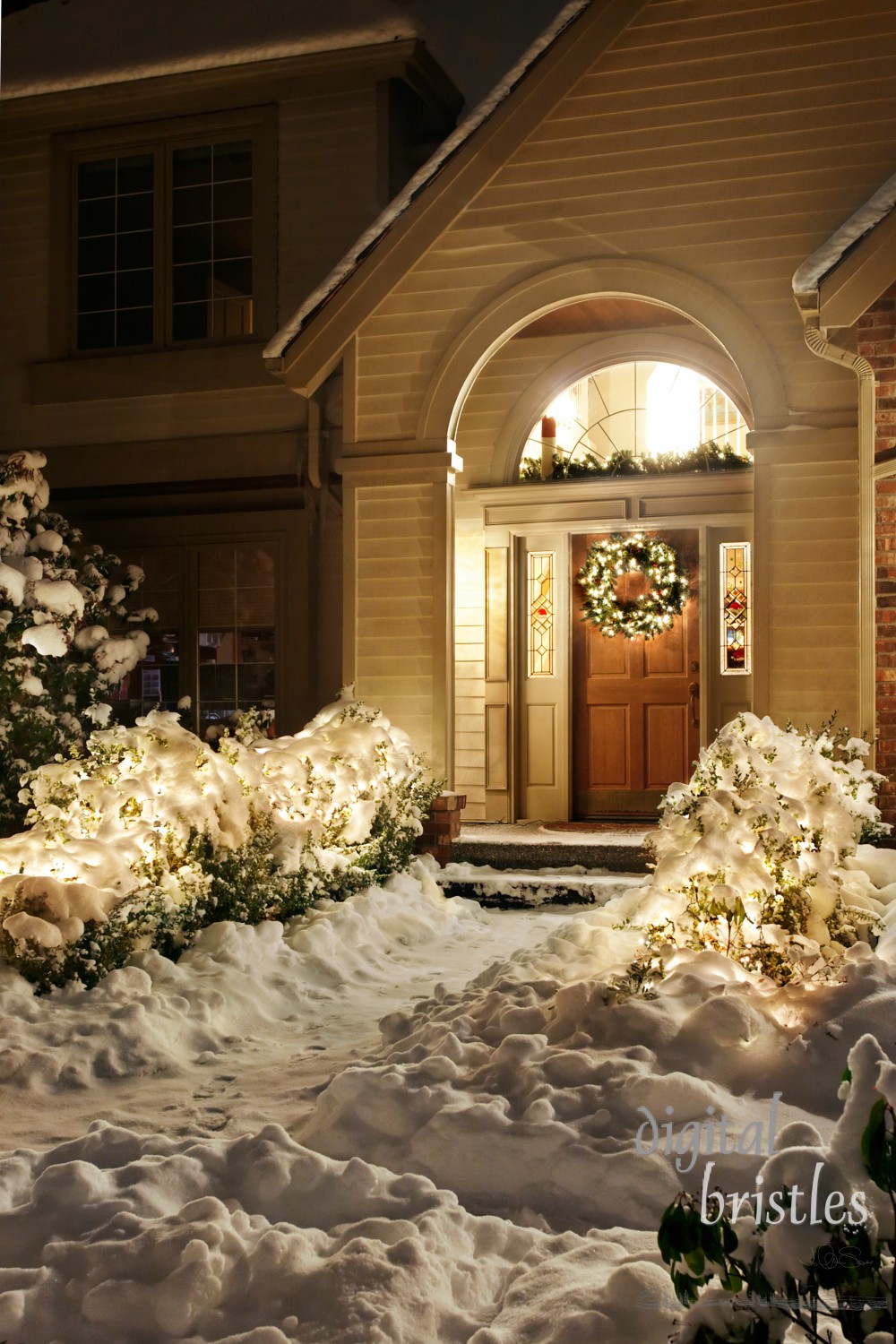 Outside Christmas lights line path to a front door on a snowy evening