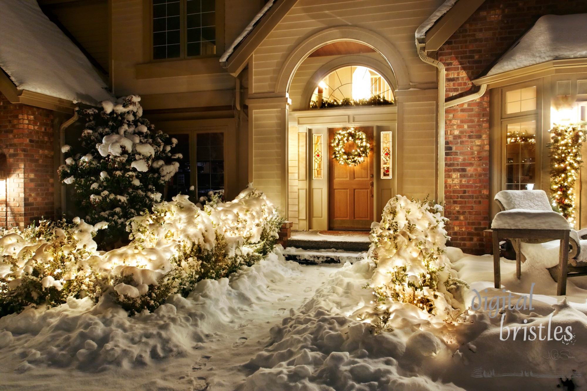 Outside Christmas lights line path to a front door on a snowy evening