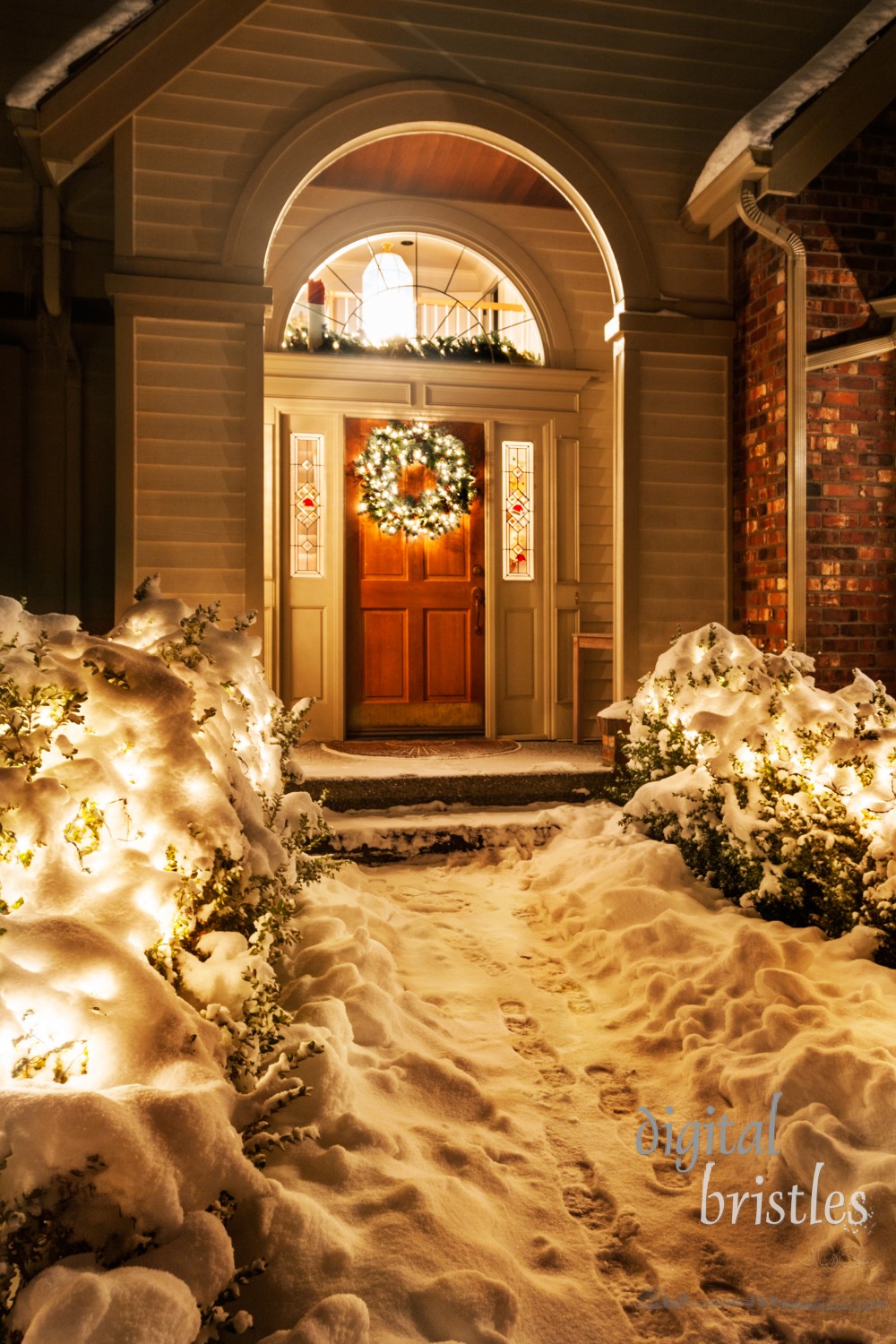 Outside Christmas lights line path to a front door on a snowy winter night