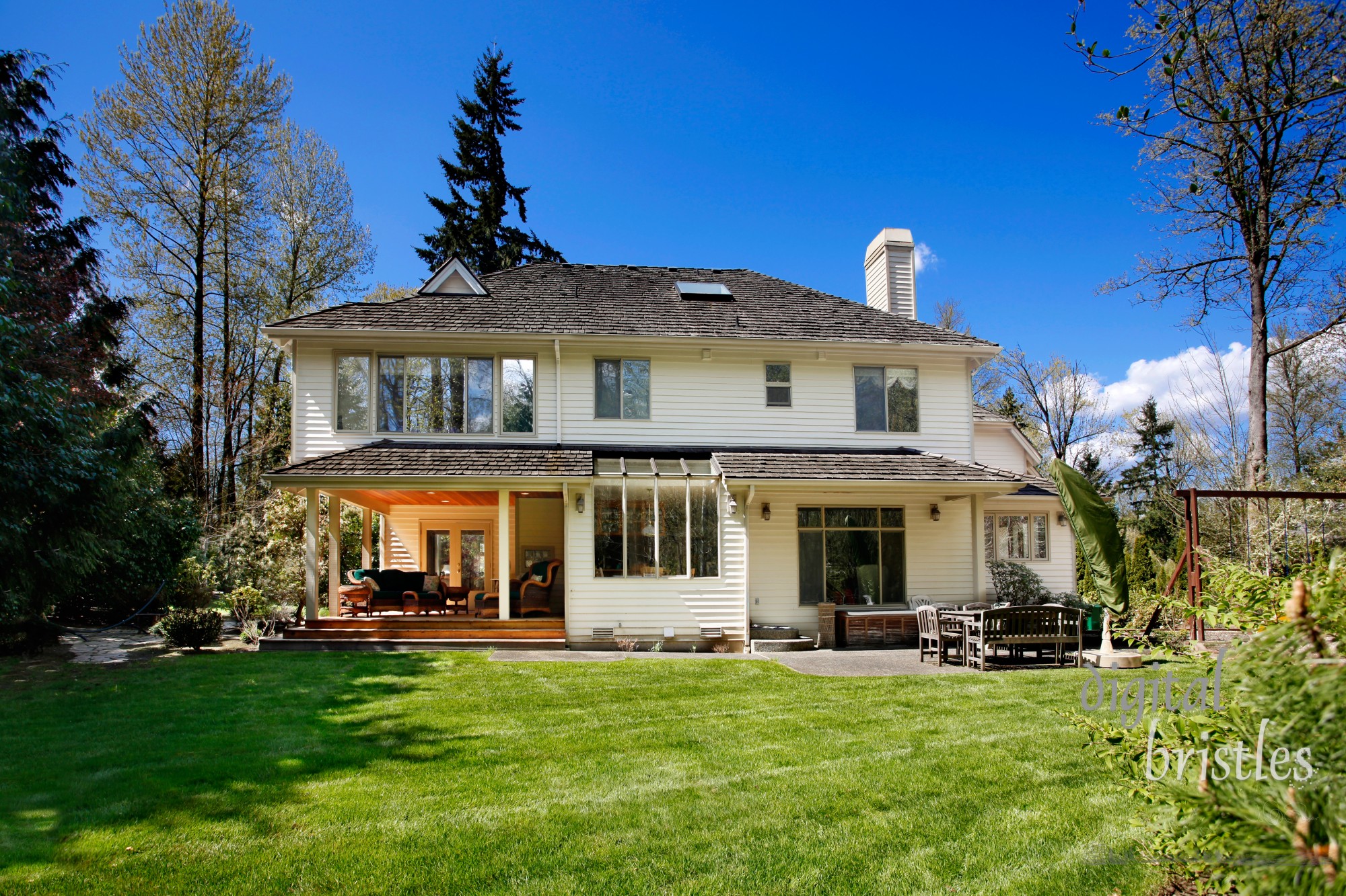 Suburban home several years after the remodeling is complete. Roof has weathered to match existing roof and stone patio installed by the covered deck.