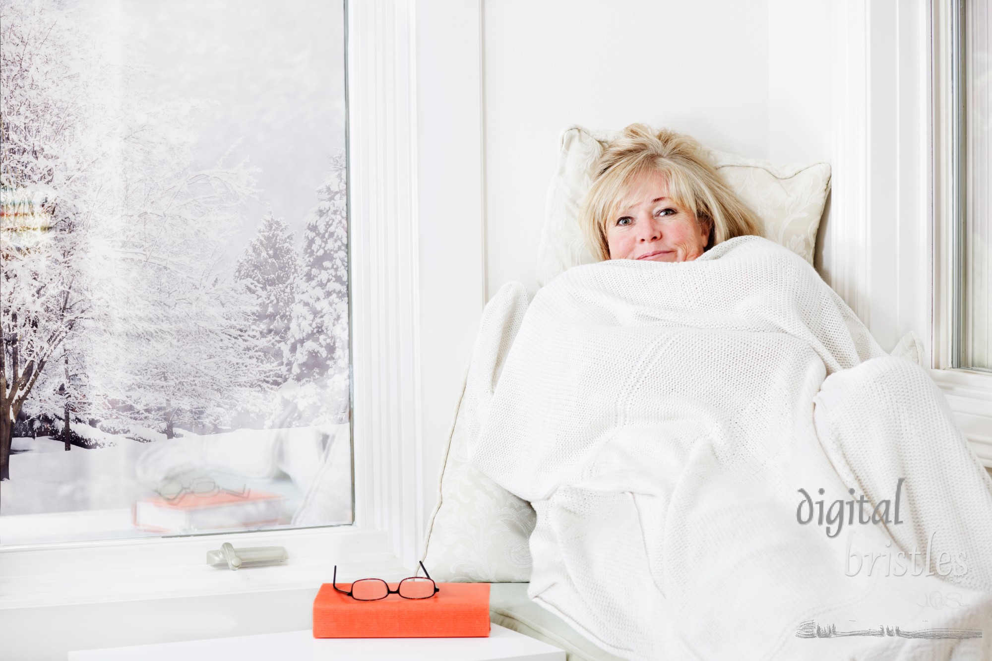 Mature woman lying down & smiling from under a warm blanket