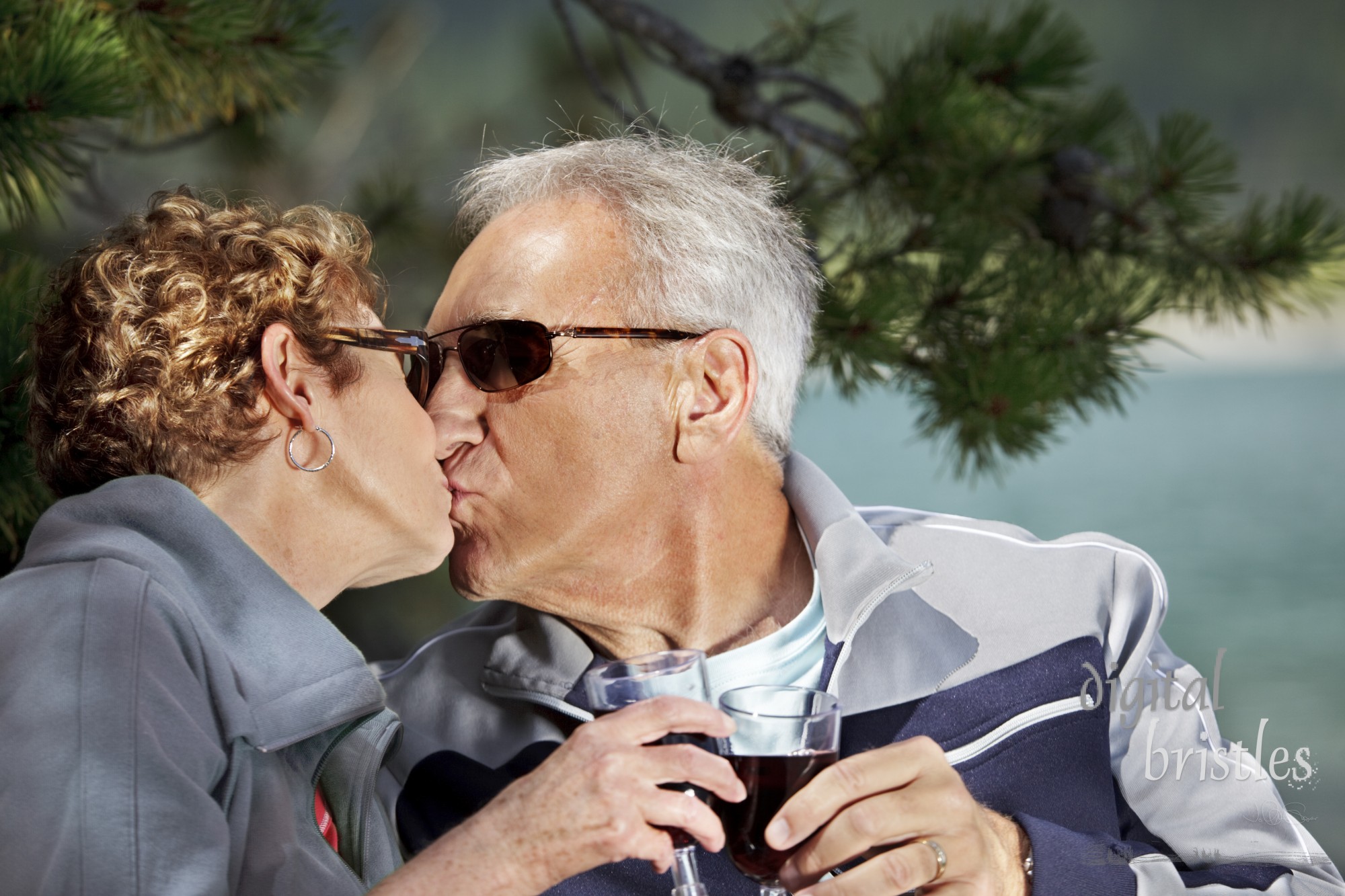 Senior couple enjoying a kiss and a glass of wine by the lake