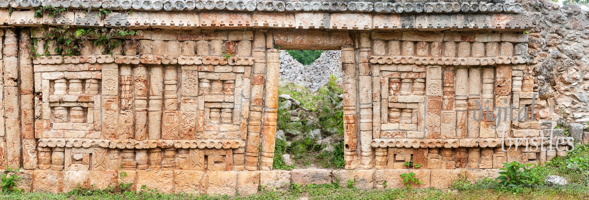 Mayan carvings in a decorated stone wall with embedded columns and doorway at Labna, Mexico