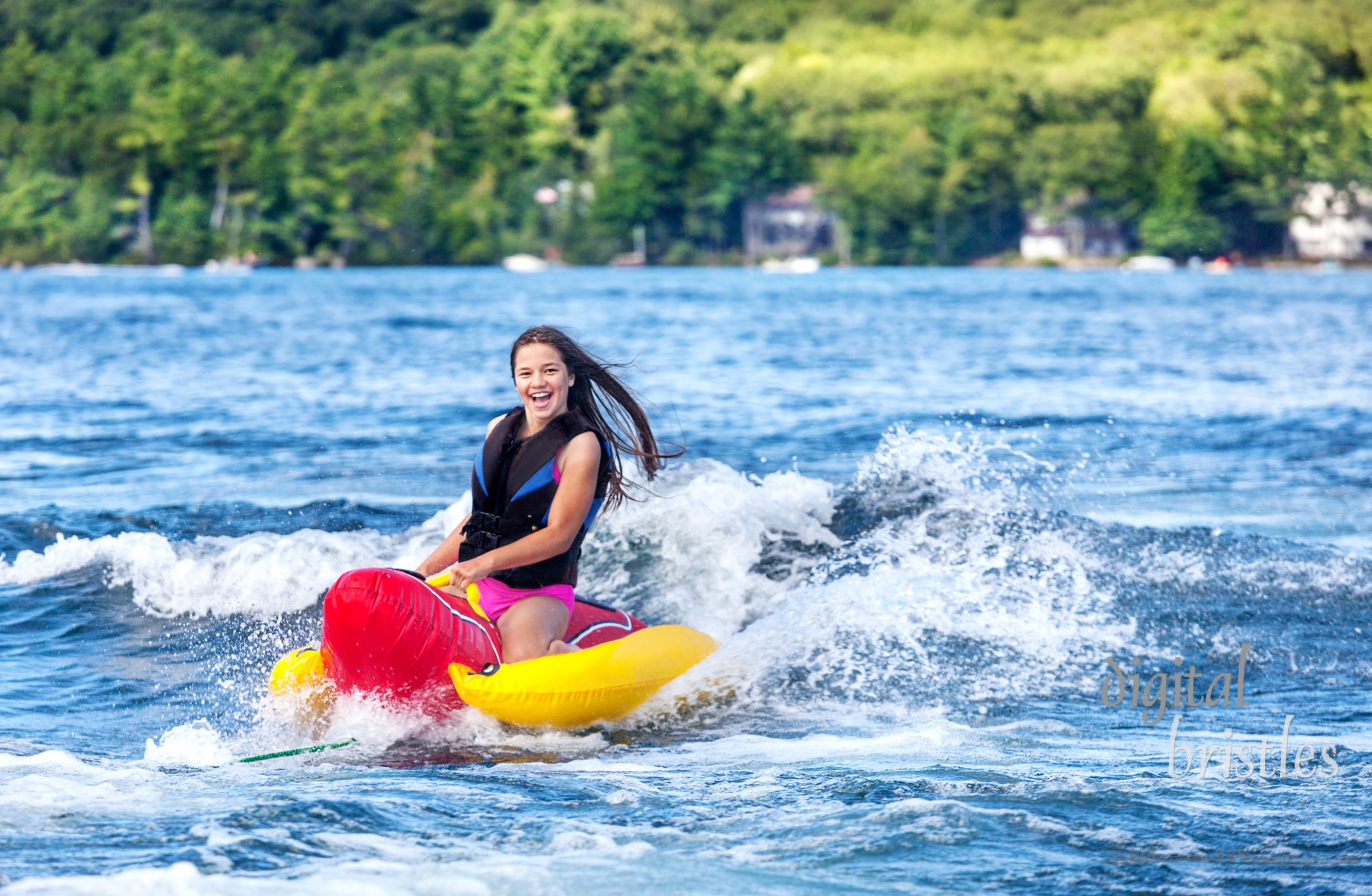 Happy young girl speeds across a lake on an inflatable on a summer day