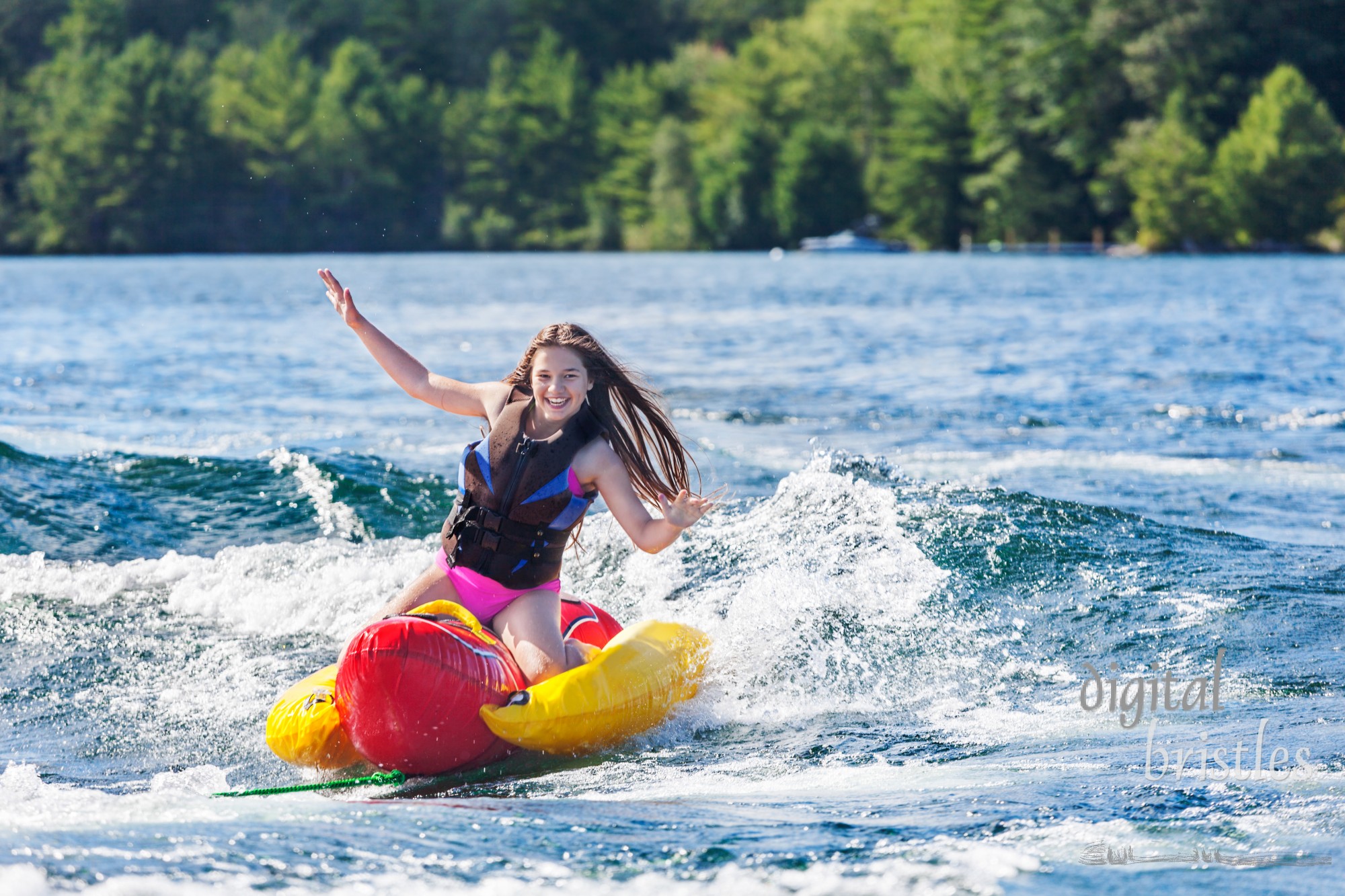 Laughing young girl speeds across a lake, hands in the air, on an inflatable on a summer day