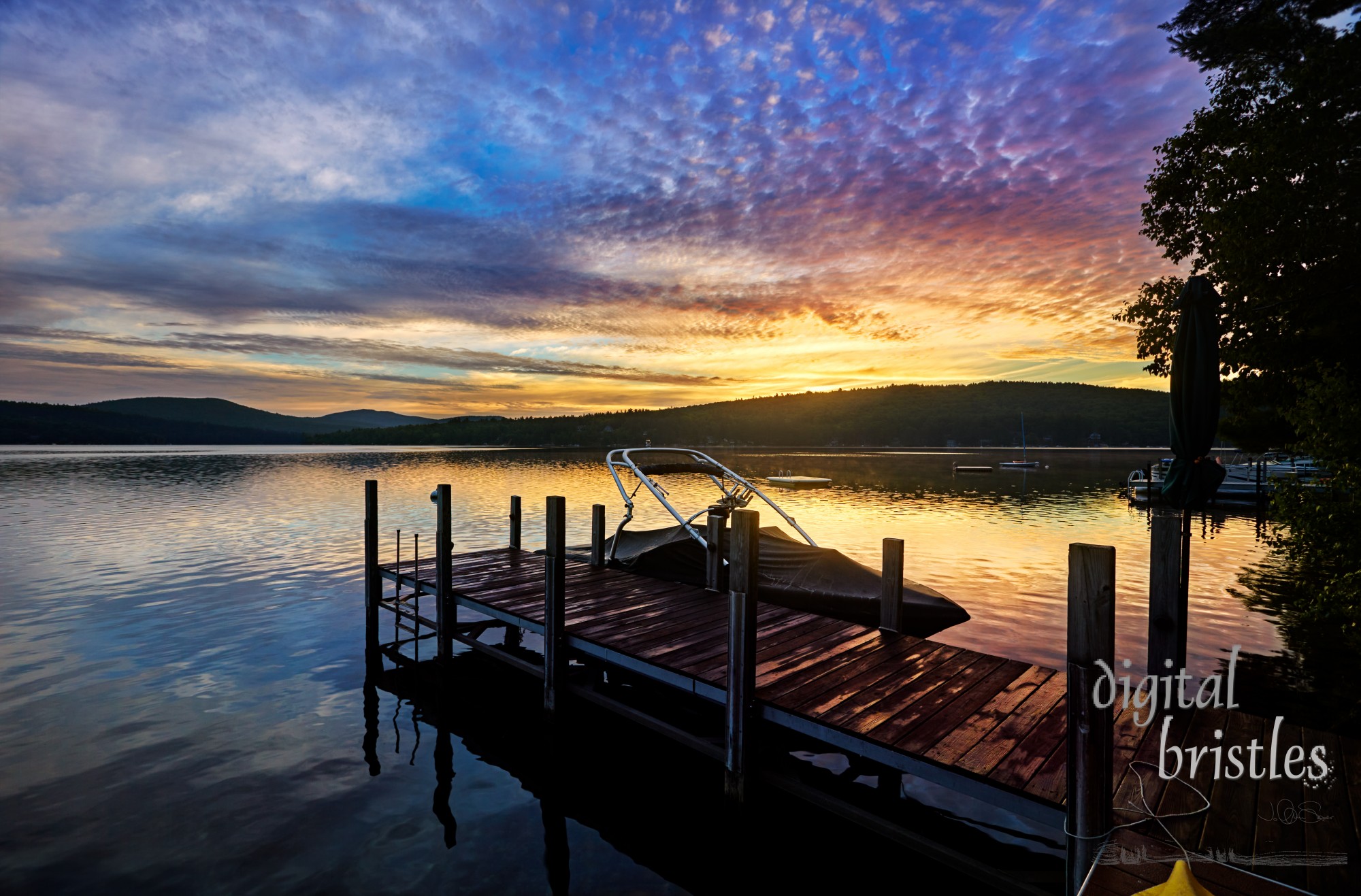 Minutes before sunrise, clouds light up with pinks and yellows over a New Hampshire lake