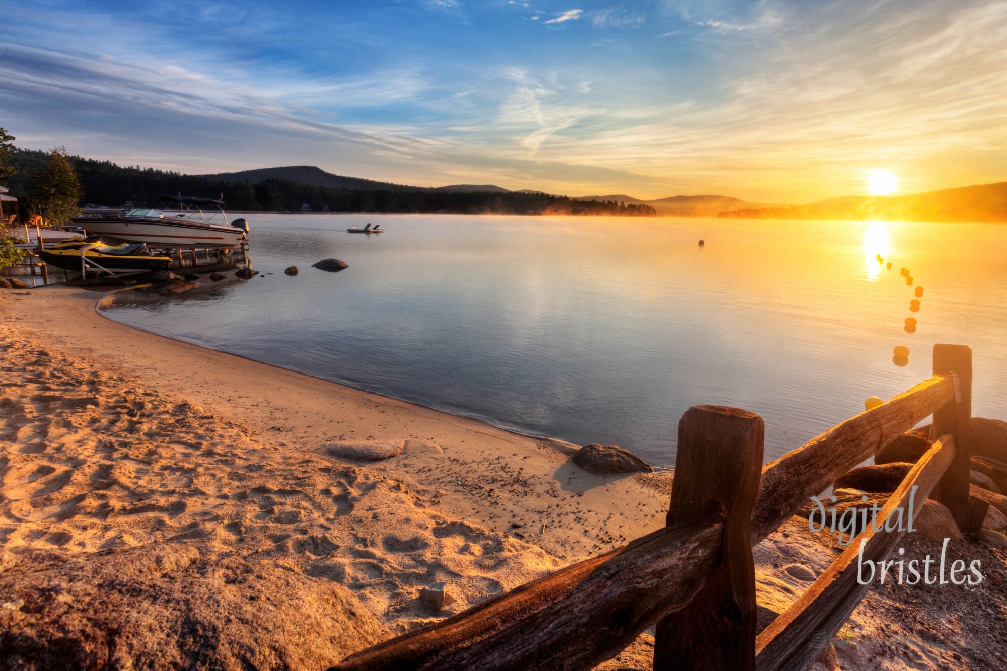 Mist rises from Merrymeeting Lake, as seen from the beach by the marina boat launch, New Durham, New Hampshire right after sunrise on a summer morning