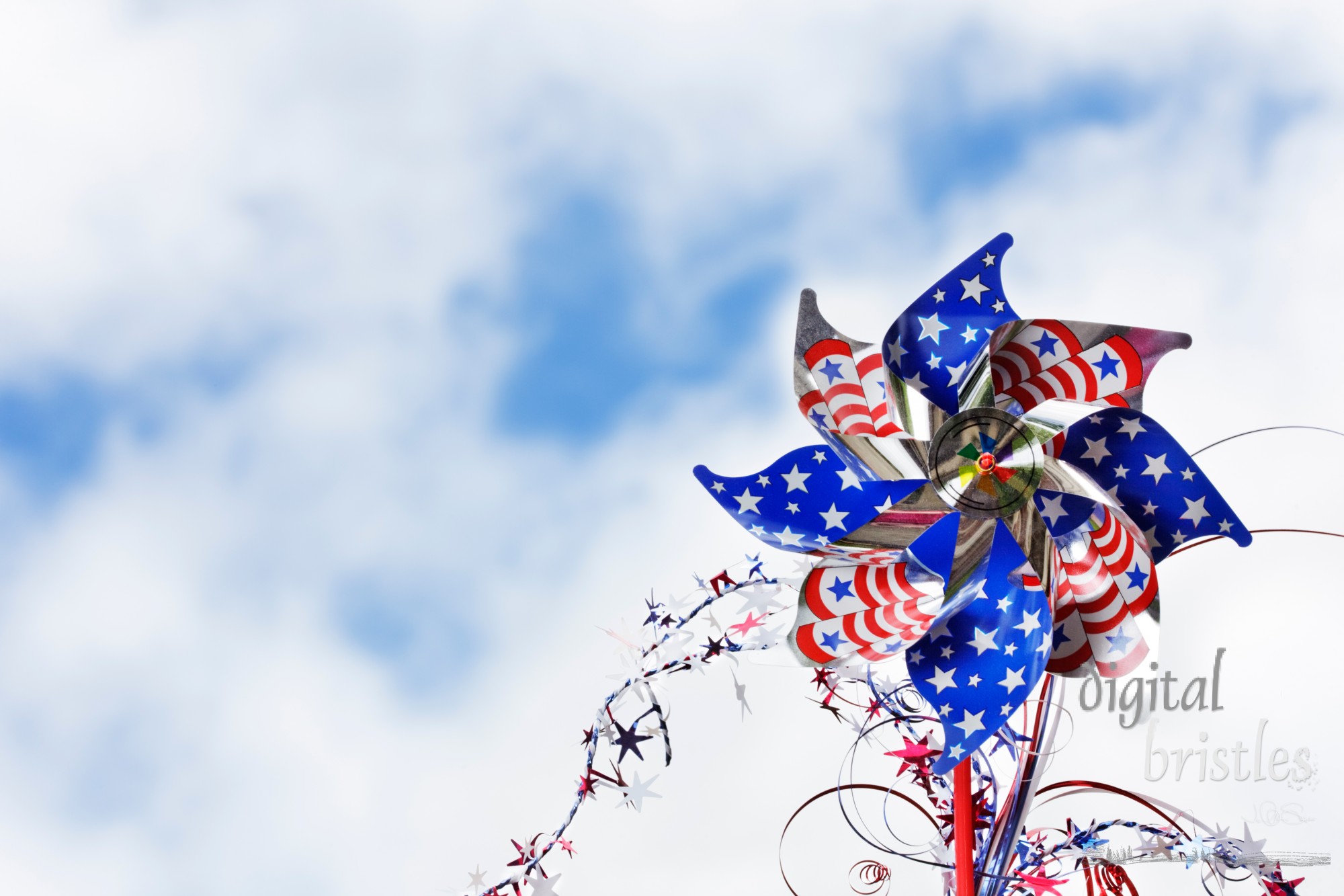 Stars & stripes pinwheel with spray of stars against a summery sky