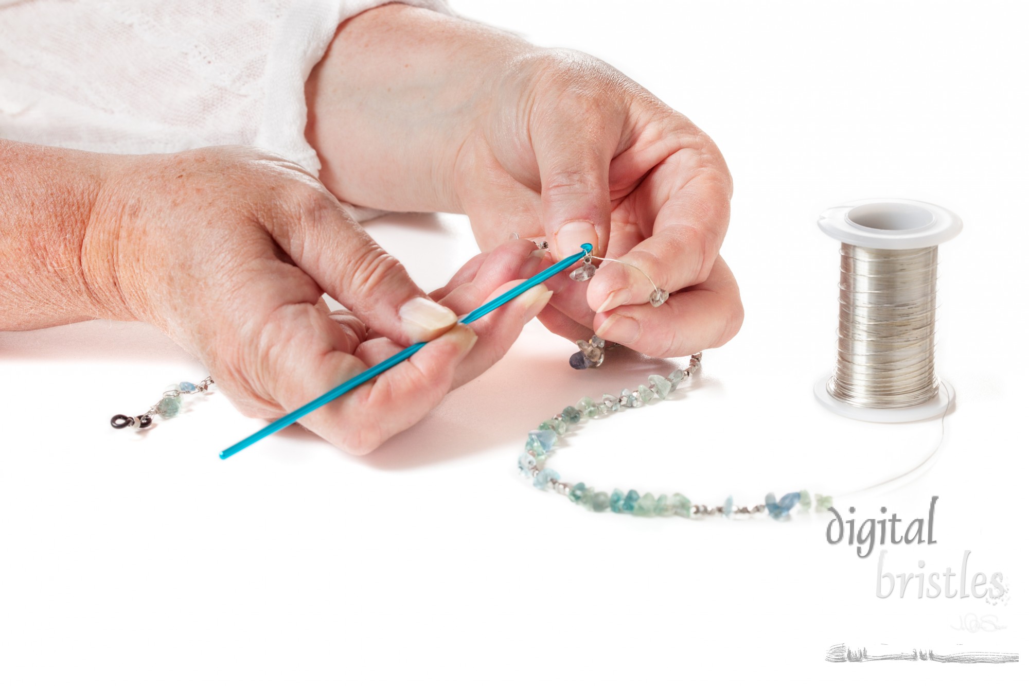 Mature woman's hands crocheting a wire eyeglass chain with blue-green beads