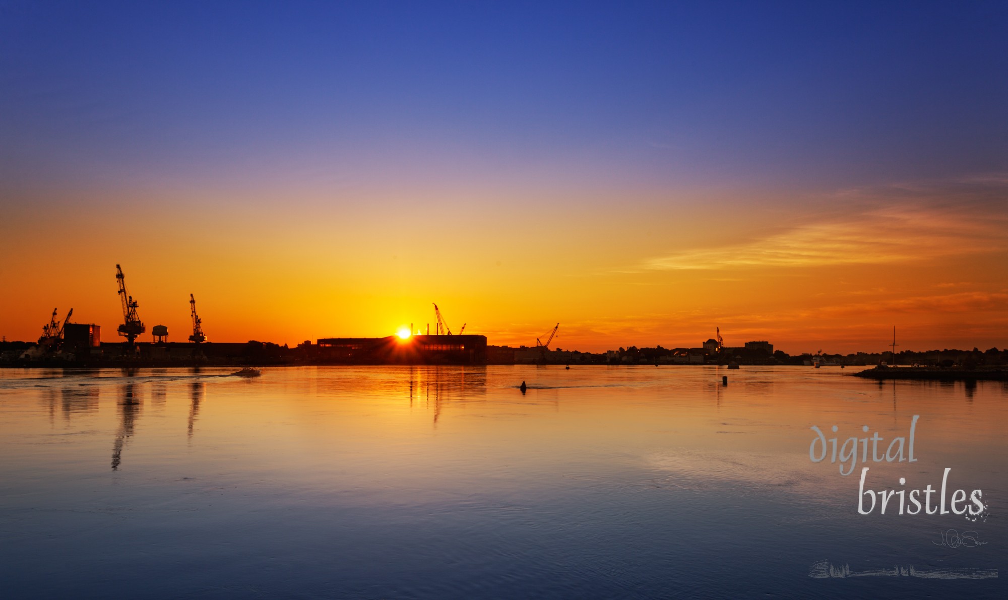 Piscataqua River, Portsmouth, New Hampshire with the sun rising behind the Navy Yard buildings in Kittery, Maine.