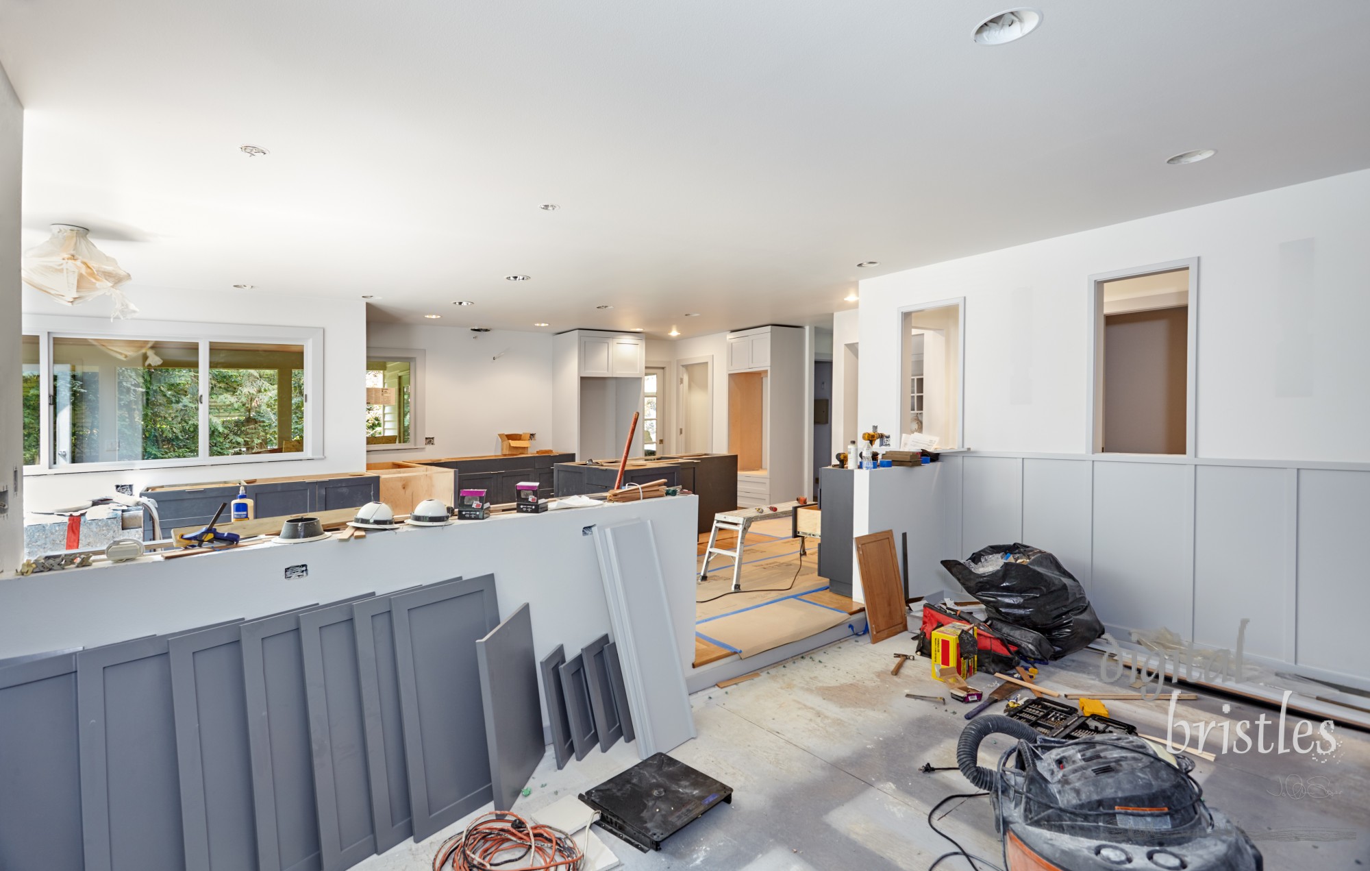 Painted cabinet doors, shelves, tools, lights, and trash bags decorate kitchen and family room during an extensive remodel