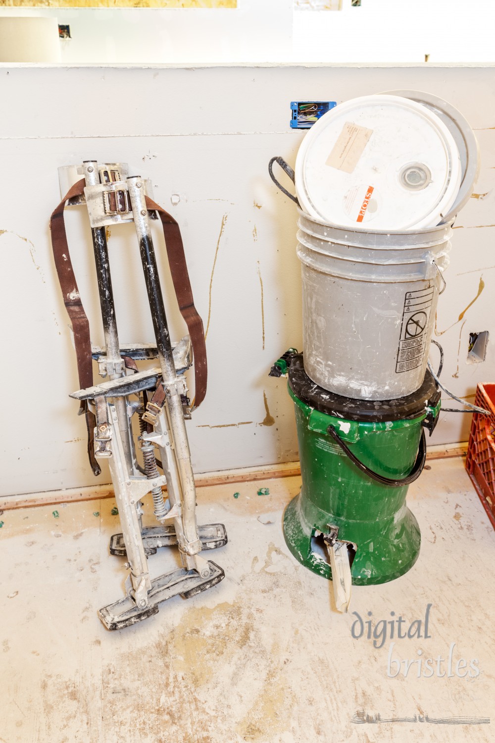 Drywaller's tools against unfinished pony wall, including stilts and buckets of spackle